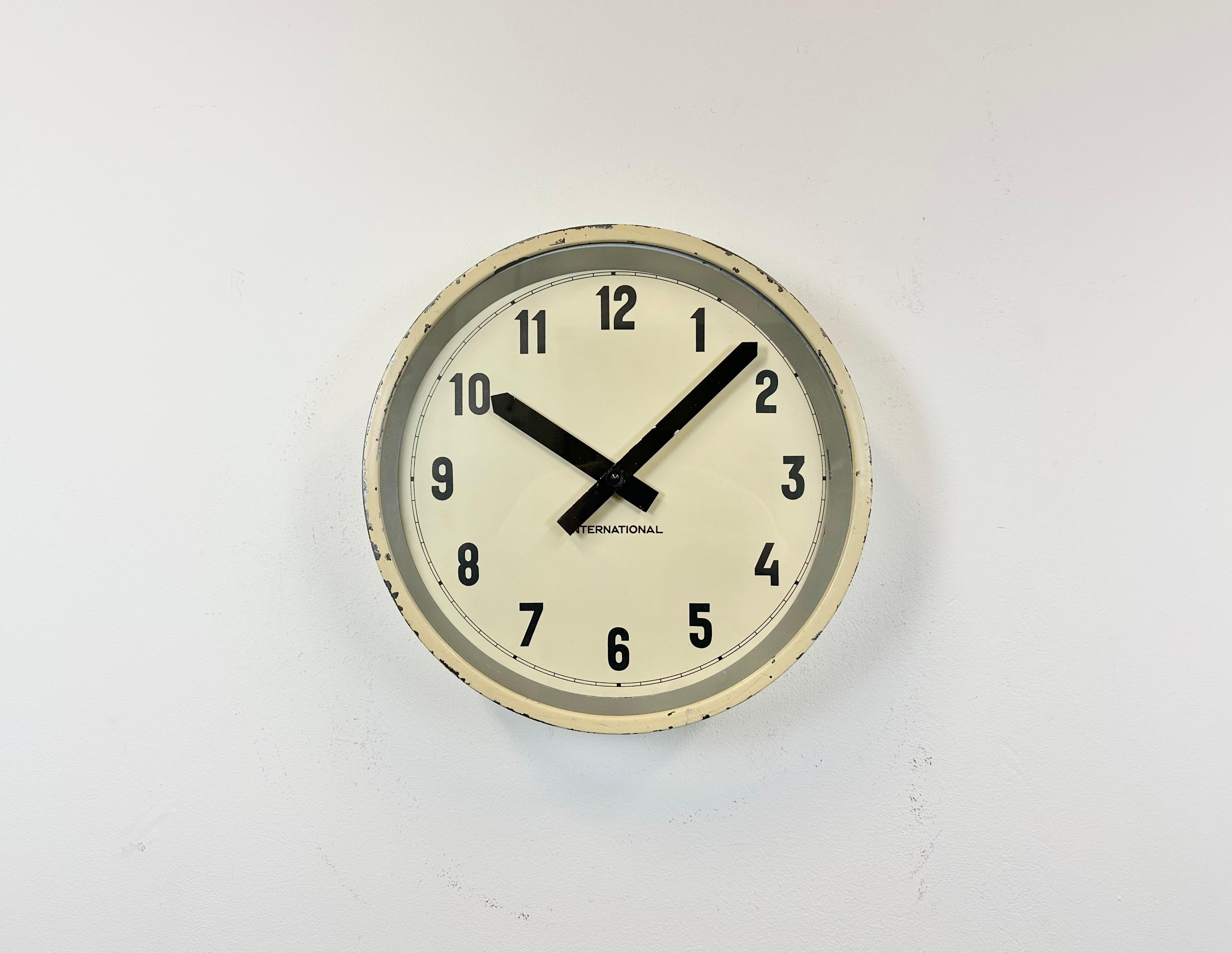 This wall clock was produced by International in Germany during the 1950s. It features a beige metal frame, an iron dial, an aluminium hands and a clear glass cover. The piece has been converted into a battery-powered clockwork and requires only one