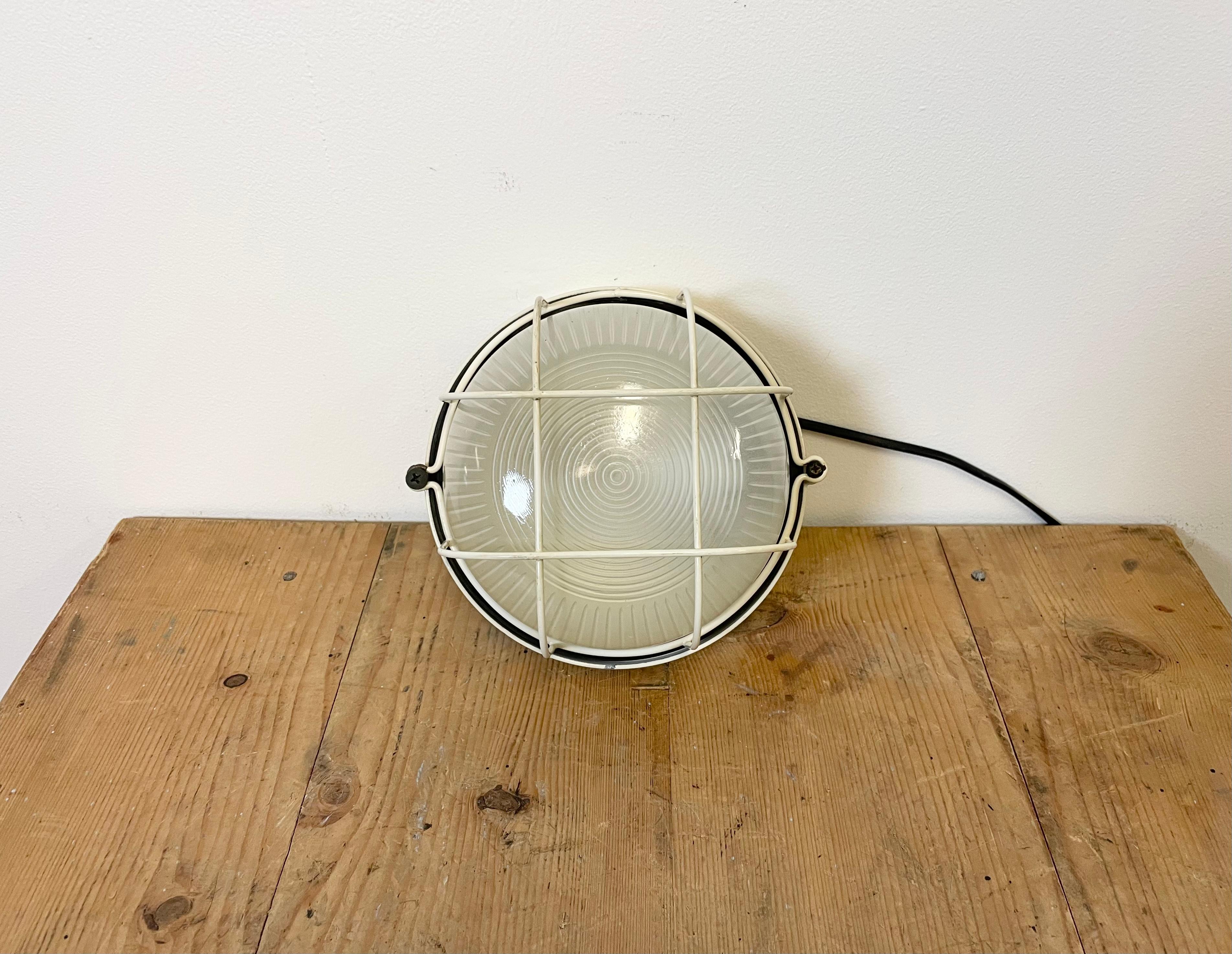 Vintage industrial iron wall lamp made in Italy during the 1970s. It features an iron body, milky stripeds curved glass cover and iron protective grid. The porcelain socket requires E 27 light bulbs. It can be also used as a ceiling lamp. Weight of