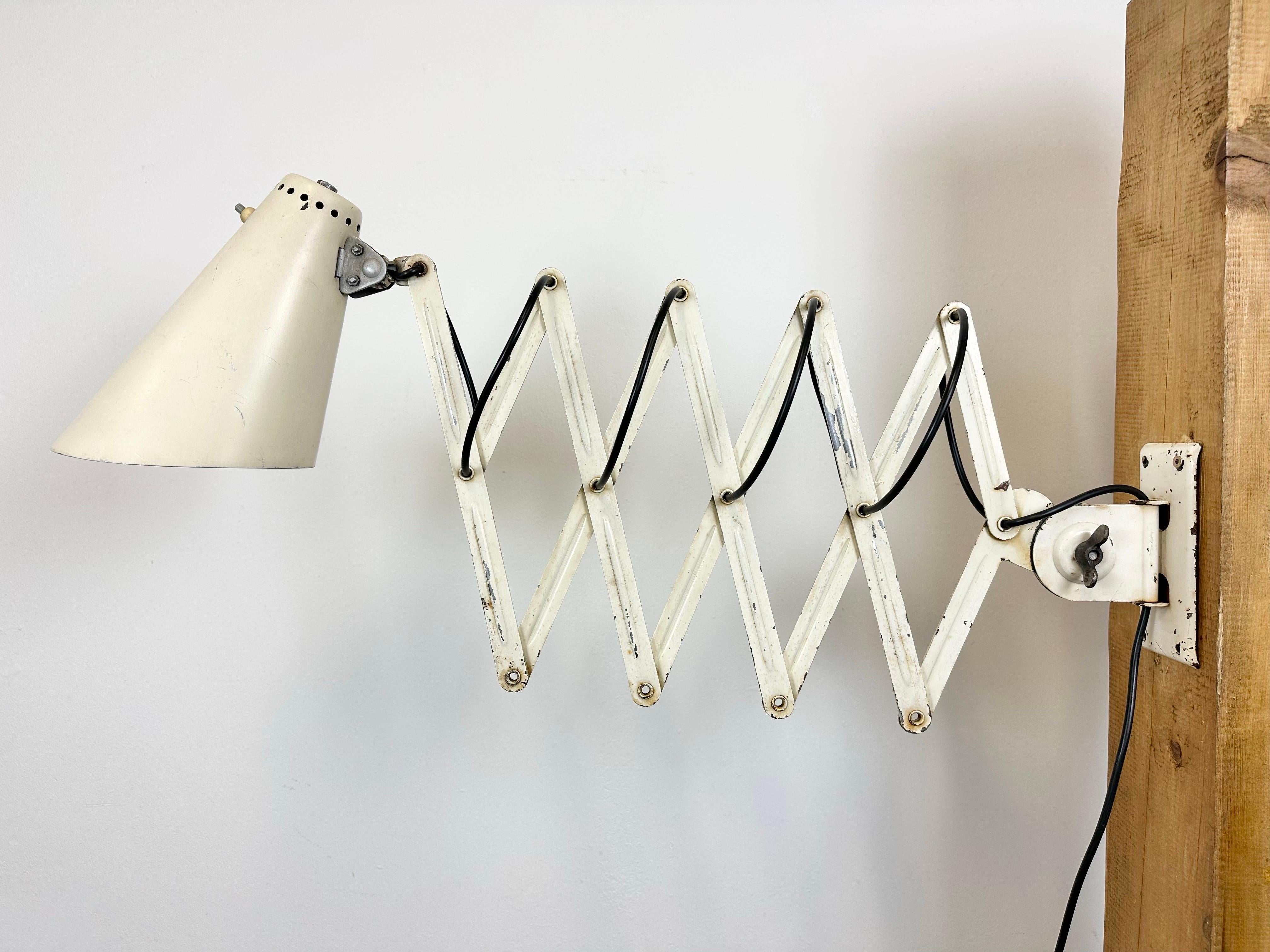 Industrial scissor wall lamp manufactured during the 1950s in former Czechoslovakia. The lamp has a metal shade. The iron scissor arm is extendable and can be turned sideways. Original swich is situated directly on shade.The socket requires E27/ E26