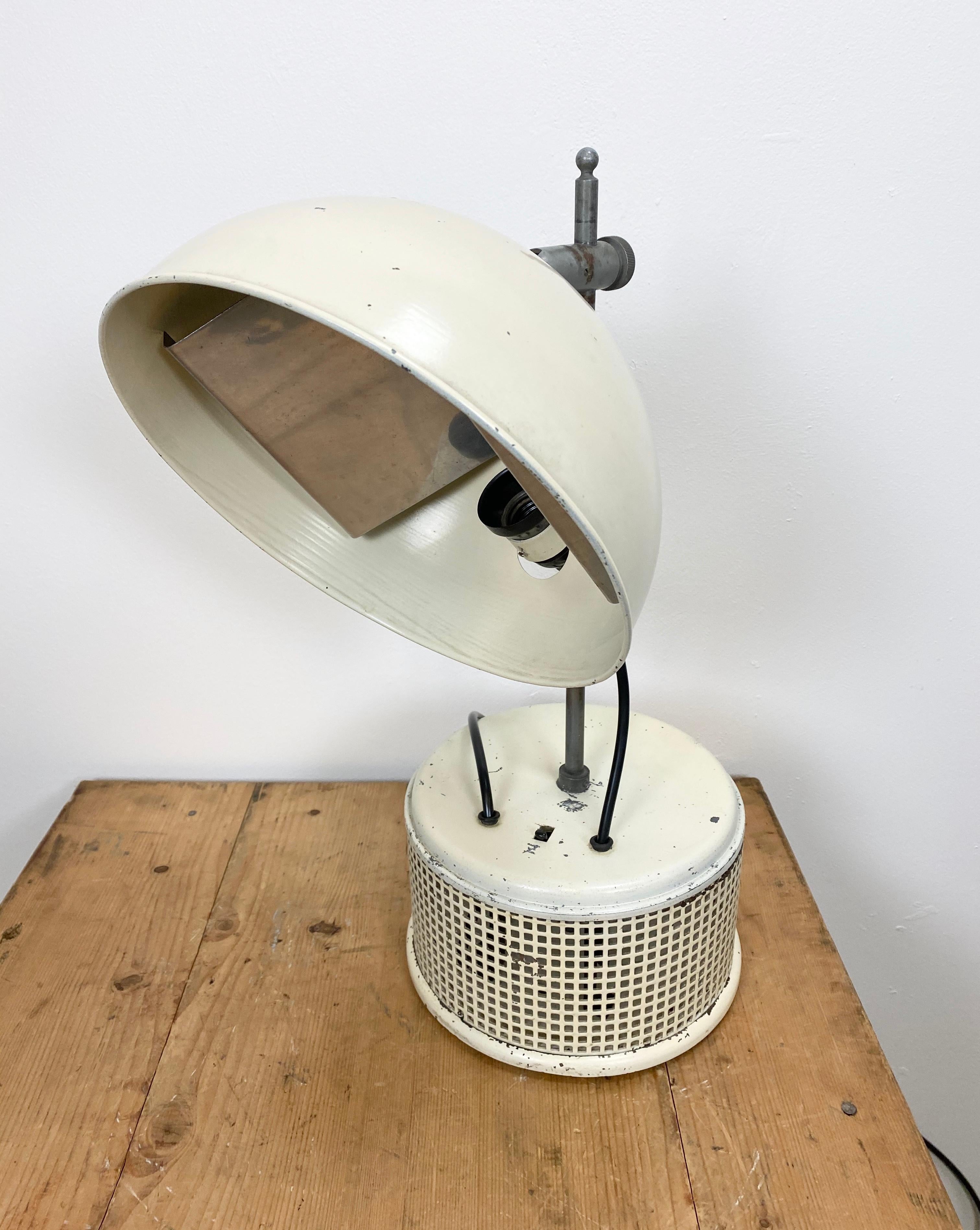 This beige industrial iron table lamp was made in former Czechoslovakia during the 1950s. It has an adjustable shade, a metal base with a switch, an original bakelite socket for E 27 light bulbs and new wire. The diameter of the lampshade is 27 cm.