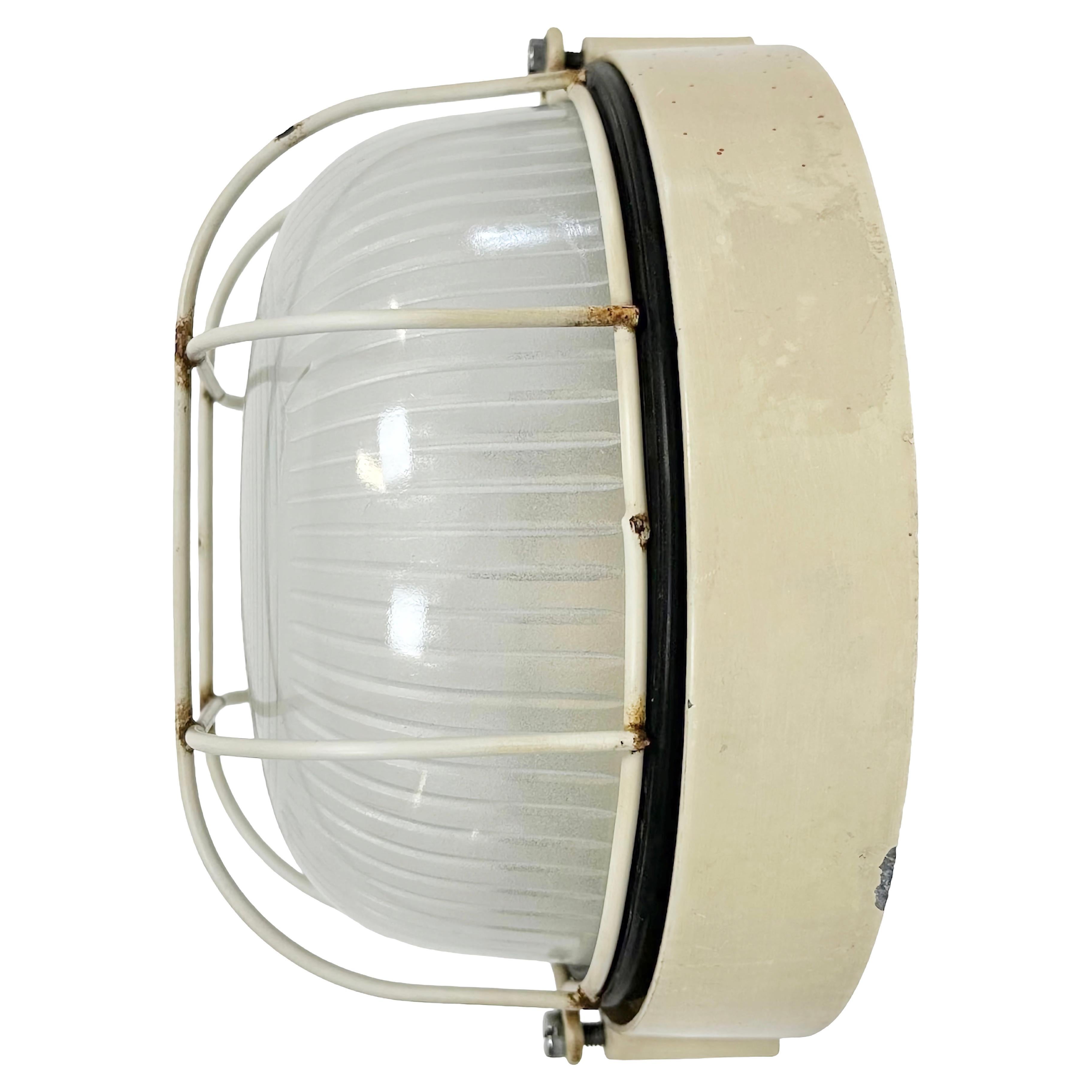 Vintage industrial iron wall lamp made in Italy during the 1970s. It features an iron body, milky stripeds curved glass cover and iron protective grid. The porcelain socket requires E 27/ E26 light bulbs. It can be also used as a ceiling lamp.