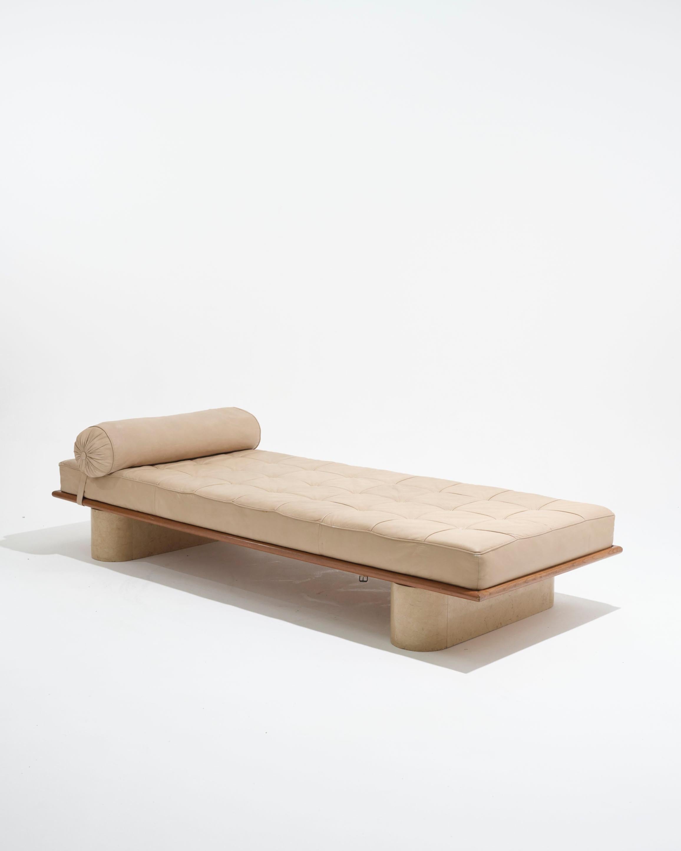 Lit de jour des années 1980 combinant le cuir, le bois et le travertin. Matelas en cuir beige fixé par des sangles, présentant quelques rides et signes d'utilisation. Structure en bois avec sommier à lattes apparent, pieds en travertin massif. En