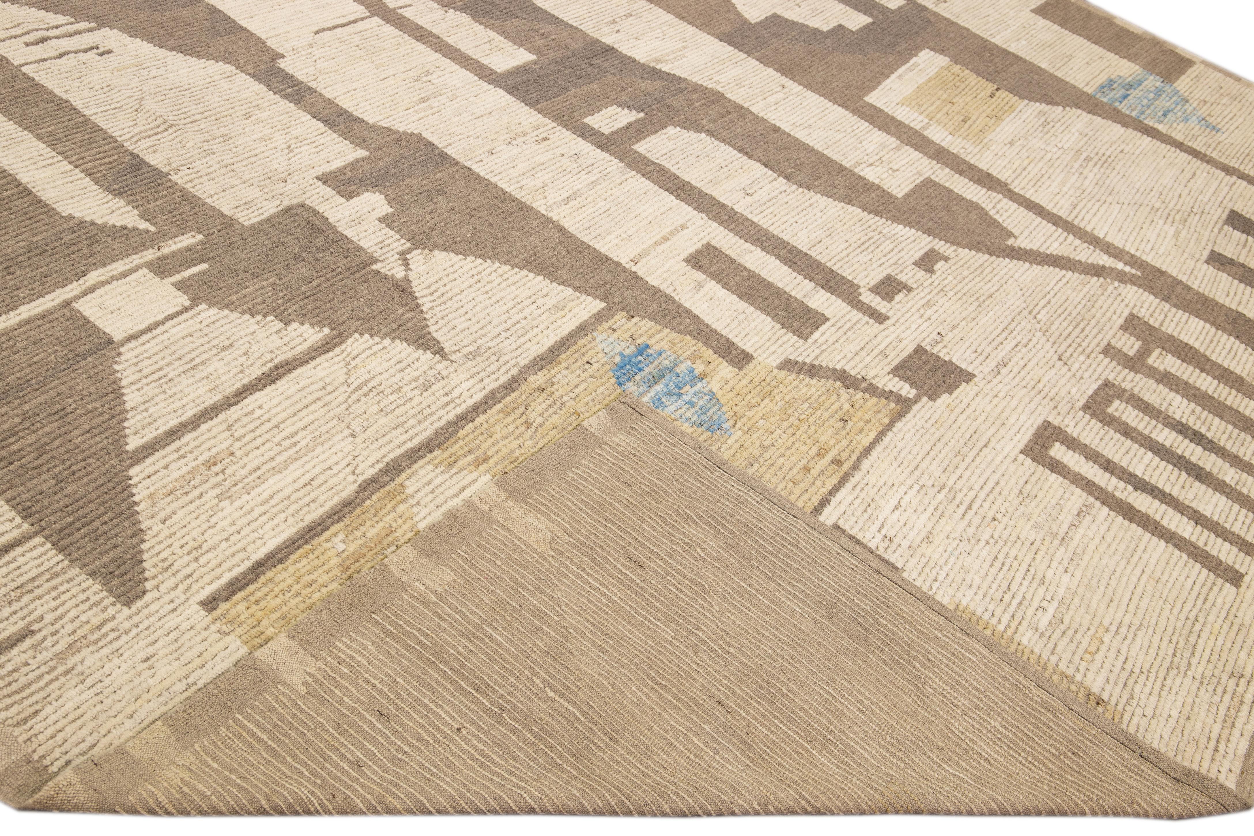 Beautiful Moroccan style handmade wool rug with a beige field. This Modern rug has brown, yellow, and blue accents featuring a gorgeous all-over abstract design.

This rug measures: 14'6