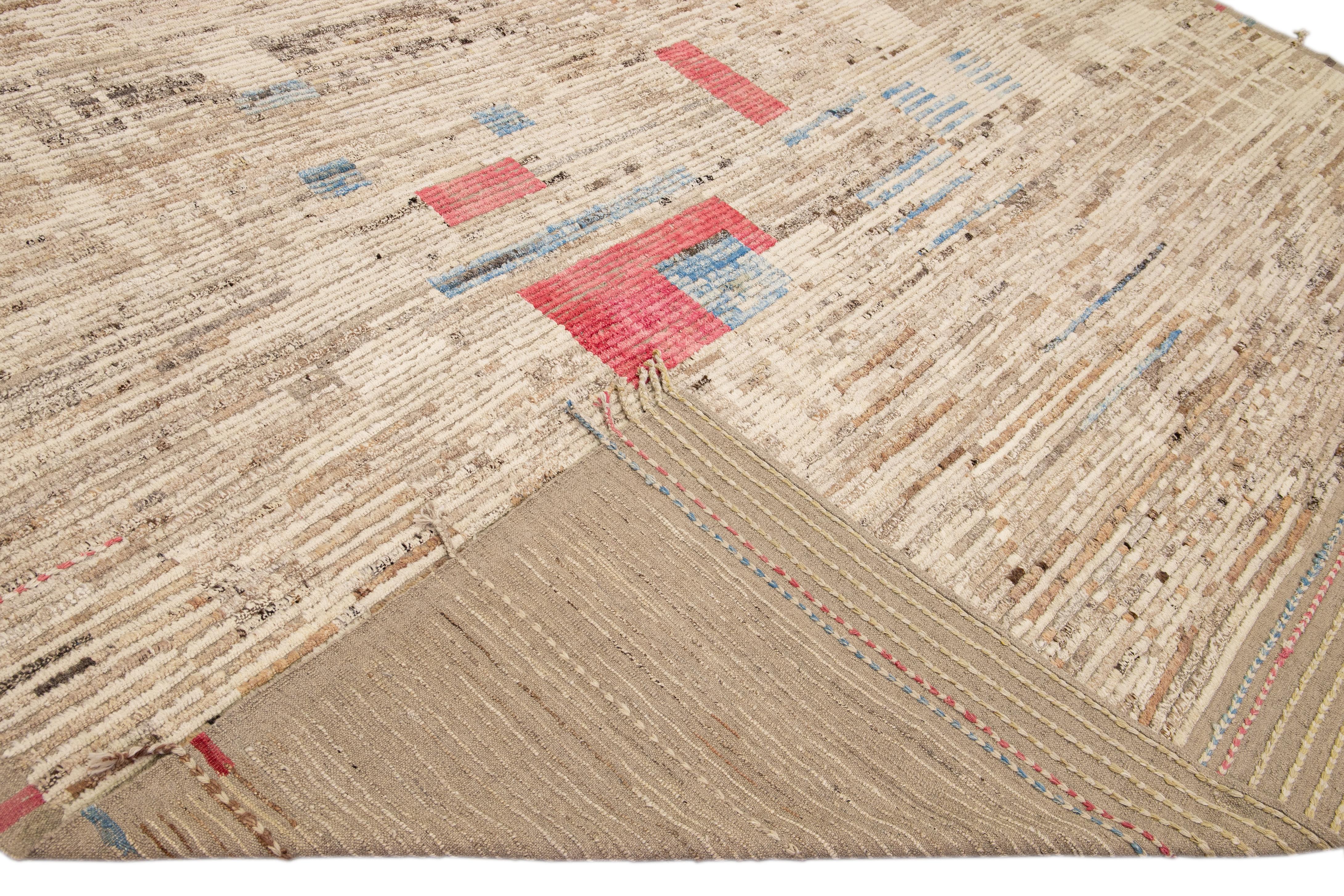Beautiful Moroccan style handmade wool rug with a beige field. This Modern rug has brown, red, and blue accents featuring a gorgeous all-over abstract design.

This rug measures: 13'6