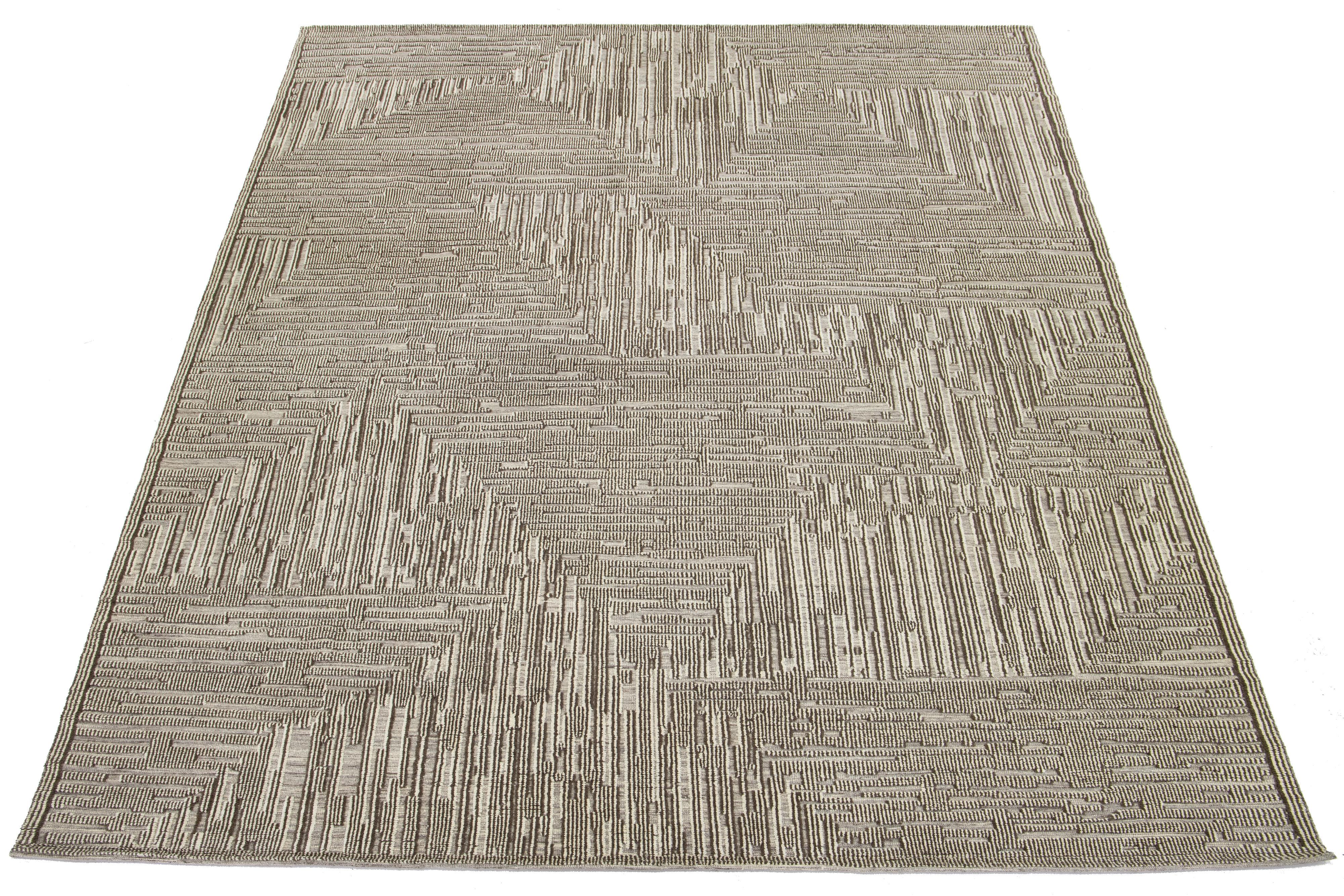 Verwandeln Sie Ihren Raum mit diesem schönen, modernen, handgeknüpften Wollteppich im marokkanischen Stil. Sein fesselndes abstraktes Design in Beige und Braun verleiht ihm Eleganz und Wärme und macht ihn zum perfekten Mittelpunkt für jeden