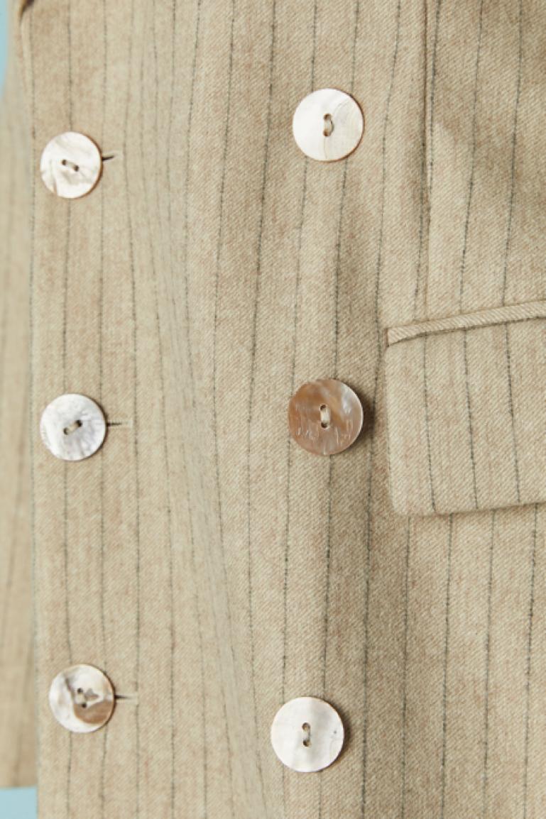 Tailleur pantalone beige con giacca a doppio petto.Composizione della fodera: 60% acetato, 40% rayon. Composizione della fodera delle maniche a righe: 100% rayon. 
Spallina sottile. Chiusura con bottoni madreperla sul centro davanti e sui polsini