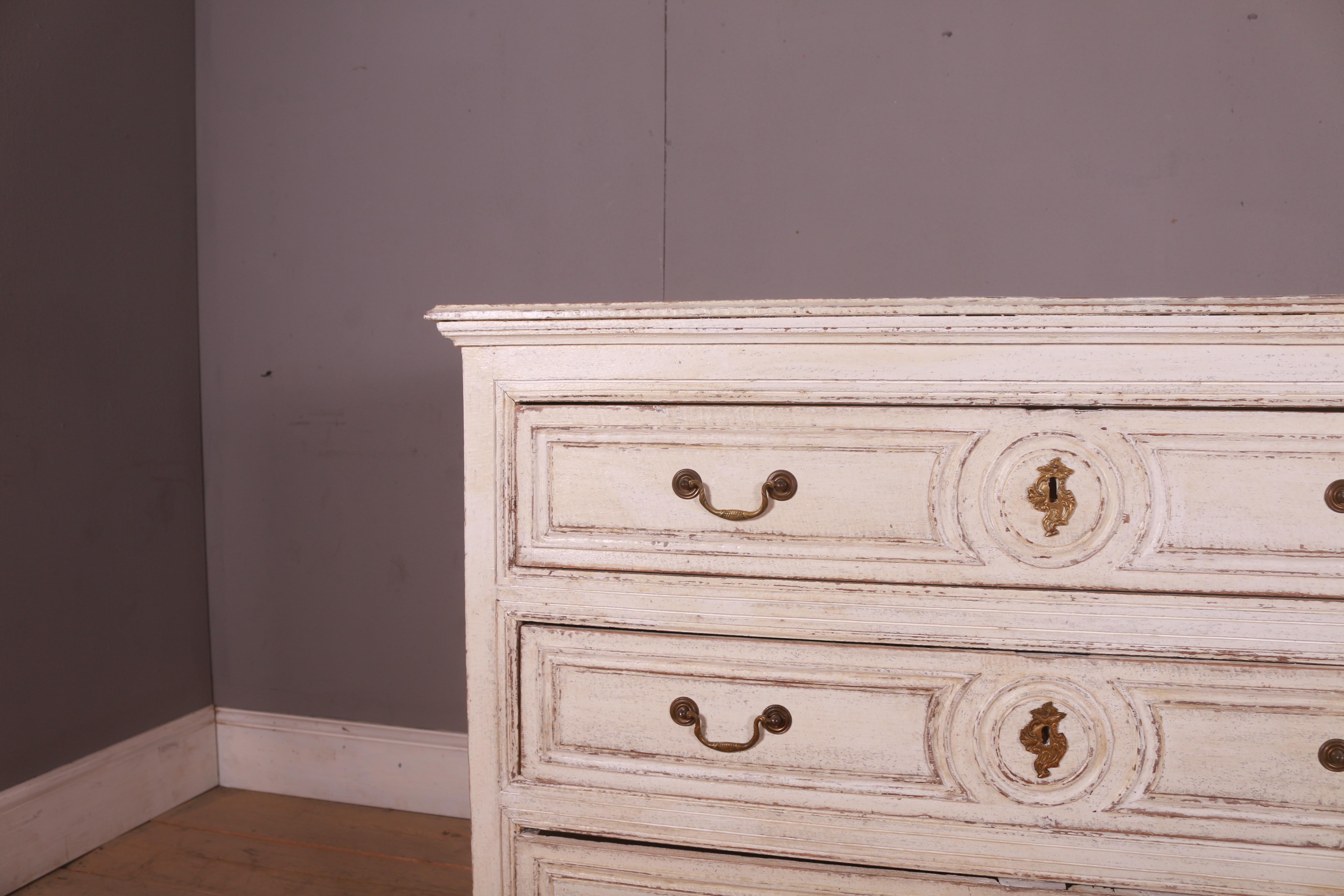 A Belgian oak commode from circa 1820 with cream/off white painted finish, three drawers and Rococo style escutcheons.  This Belgian oak commode, dating back to circa 1820, is a splendid representation of timeless elegance and functionality. The