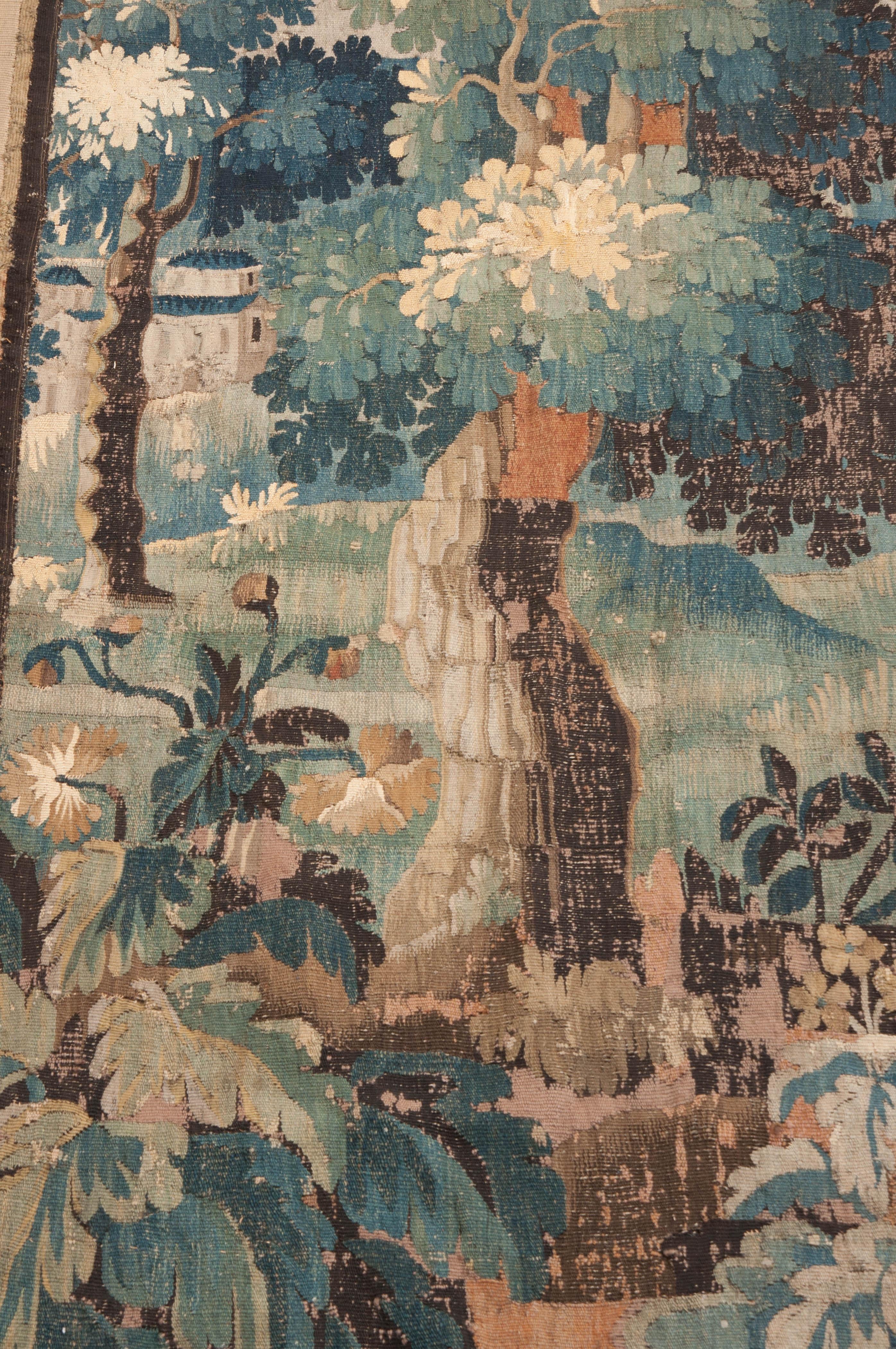 This gorgeous wool tapestry, circa 1750, is from Belgium and features a forest landscape with verdant trees and shrubbery, and having floral and foliate horizontal borders and striped vertical borders which accent its height. Time has been kind to