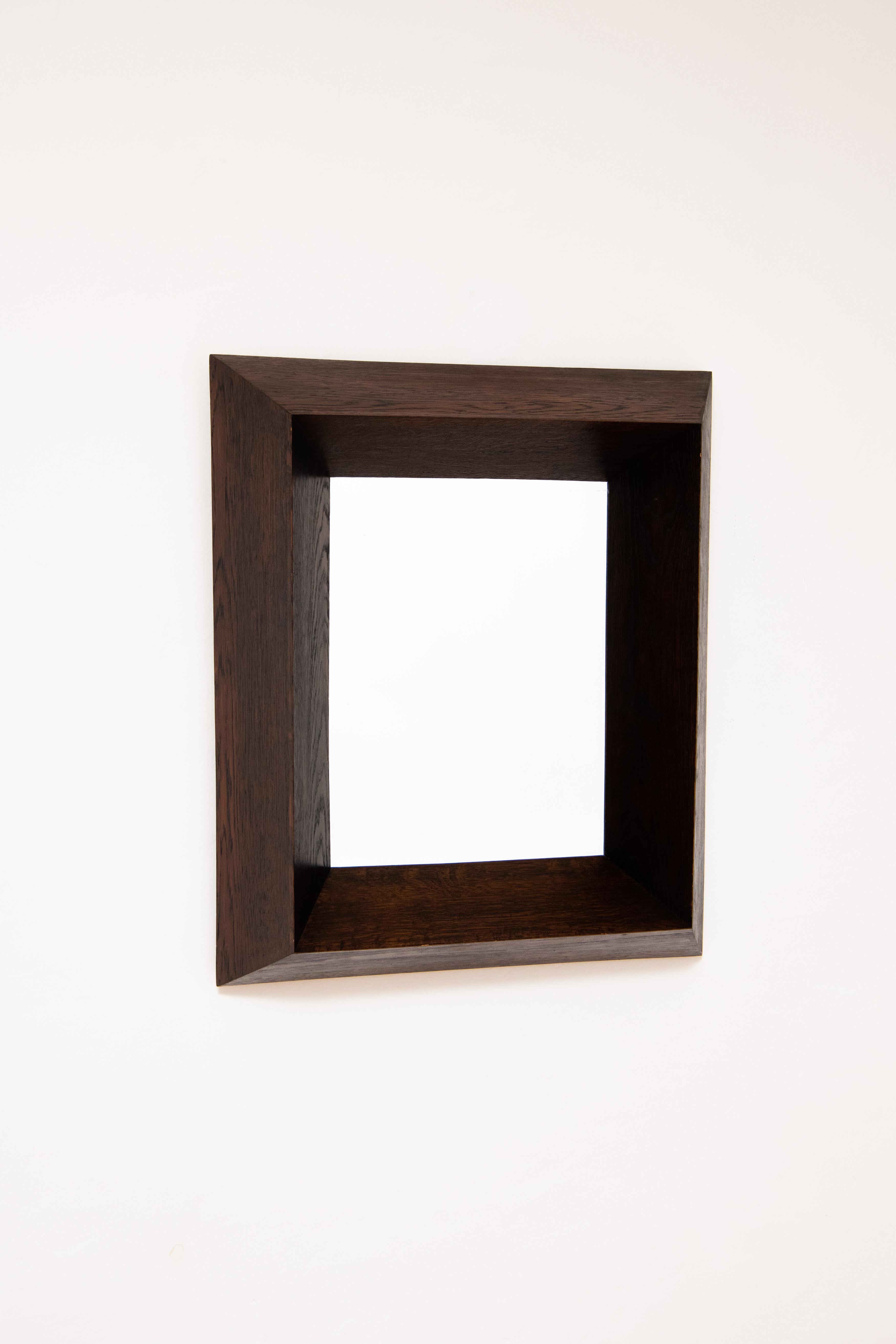A rectangular wall mirror framed with a bold, dimensional frame with a Cubist influence. The frame, which projects from the wall, is made of dark stained oak wood and is hollow for the sake of hanging on a wall. Belgian art deco circa 1930-1940.