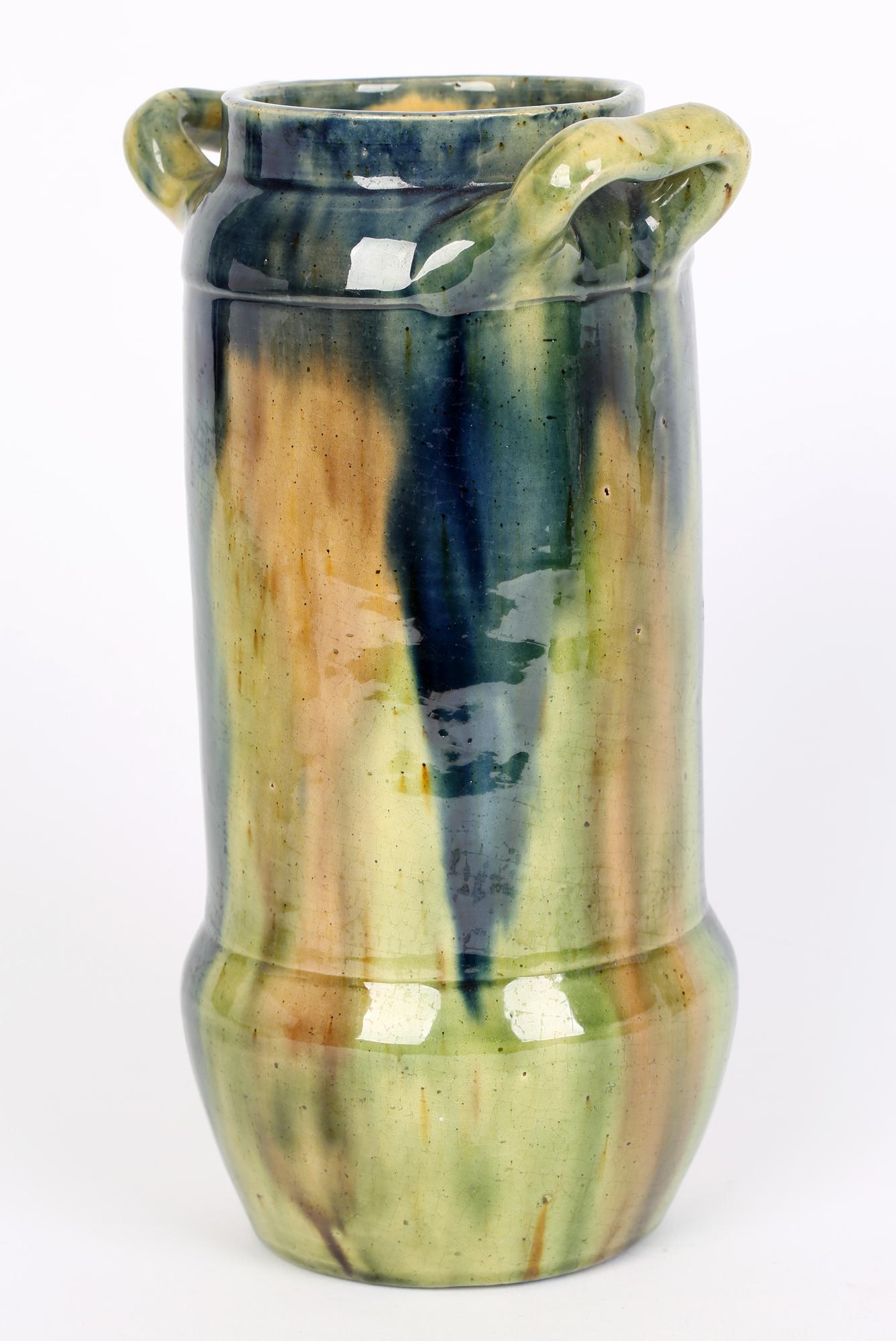 A stylish Belgian Art Nouveau twin handled art pottery vase decorated in streaked glazes dating from around 1900. The earthenware vase is of tall cylindrical shape with a rounded bowl shaped base and flat glazed foot with a rounded shoulder applied