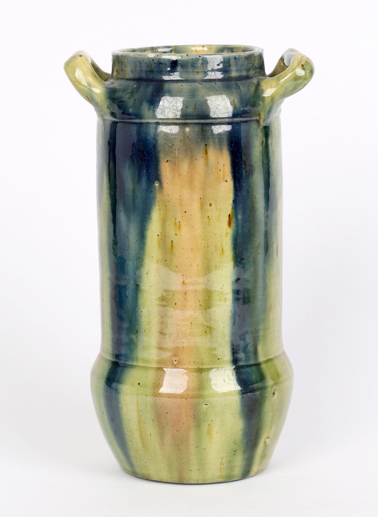 A stylish Belgian Art Nouveau twin handled art pottery vase decorated in streaked glazes dating from around 1900. The earthenware vase is of tall cylindrical shape with a rounded bowl shaped base and flat glazed foot with a rounded shoulder applied