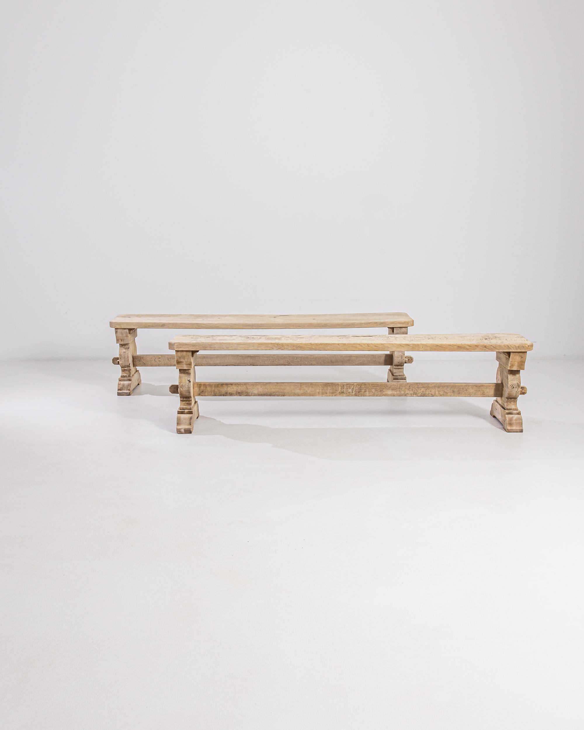 Built in 20th century Belgium, this pair of vintage oak benches have an age-old silhouette which dates back to the long tables of medieval feasts. A simple seat rests atop carved trestle legs, joined with a stretcher, providing space for multiple