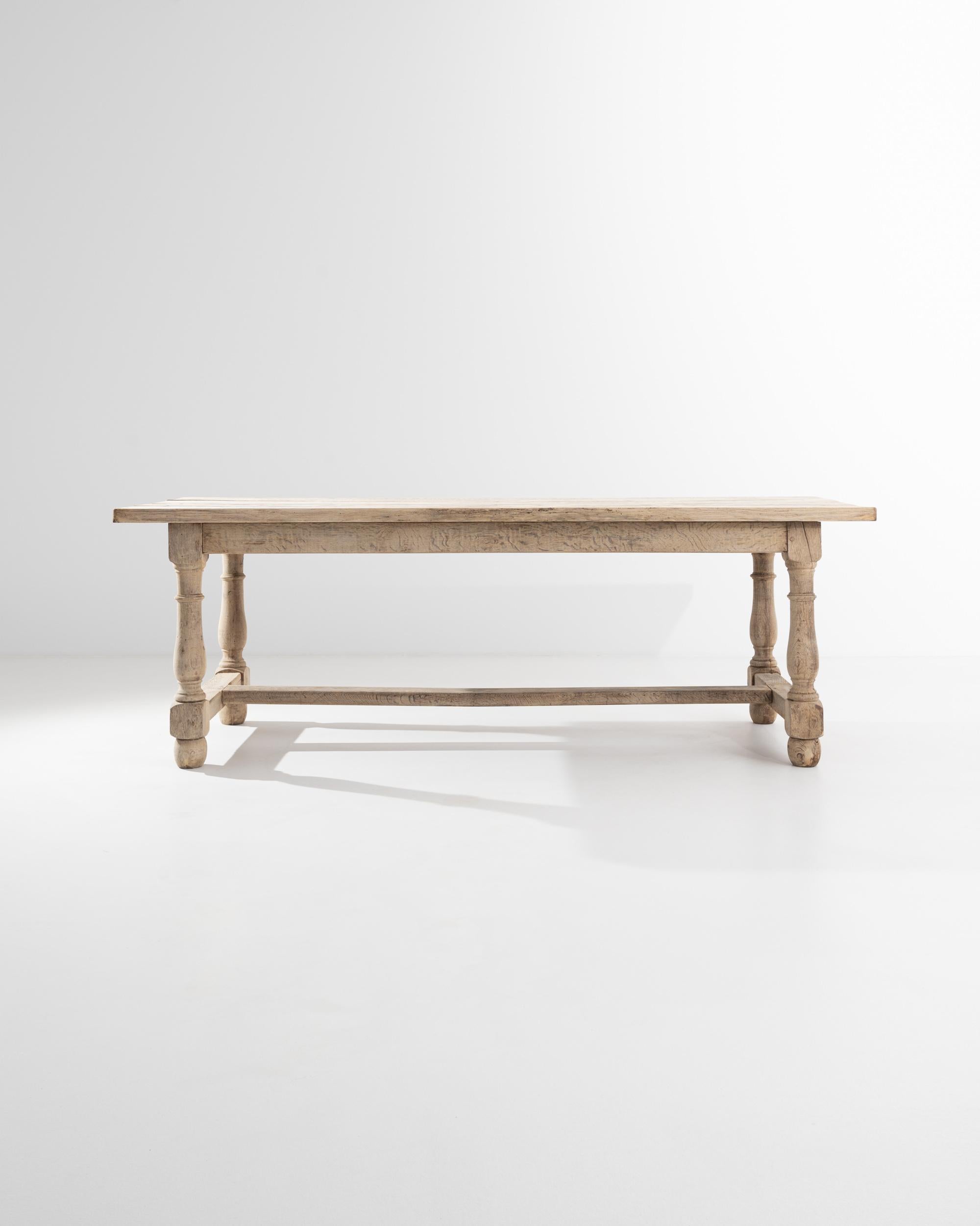A wooden dining table from the 20th century. Natural stripes of wood grain flow gracefully along the expansive, time-touched planks that compose the top and conjoining structures of this elegant dining table. Its construction is forthright and