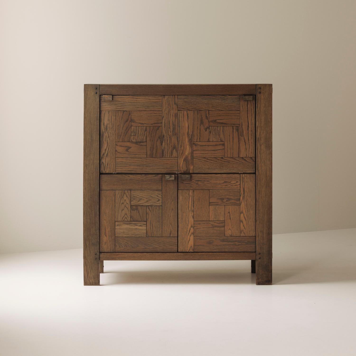 A striking example of Belgian Brutalist design, this “Modena” highboard by Frans Defour was produced in the 1970s by Defour, Belgium. Made out from solid stained oak, it features a bold graphical parquetry pattern across the doors that emphasizes