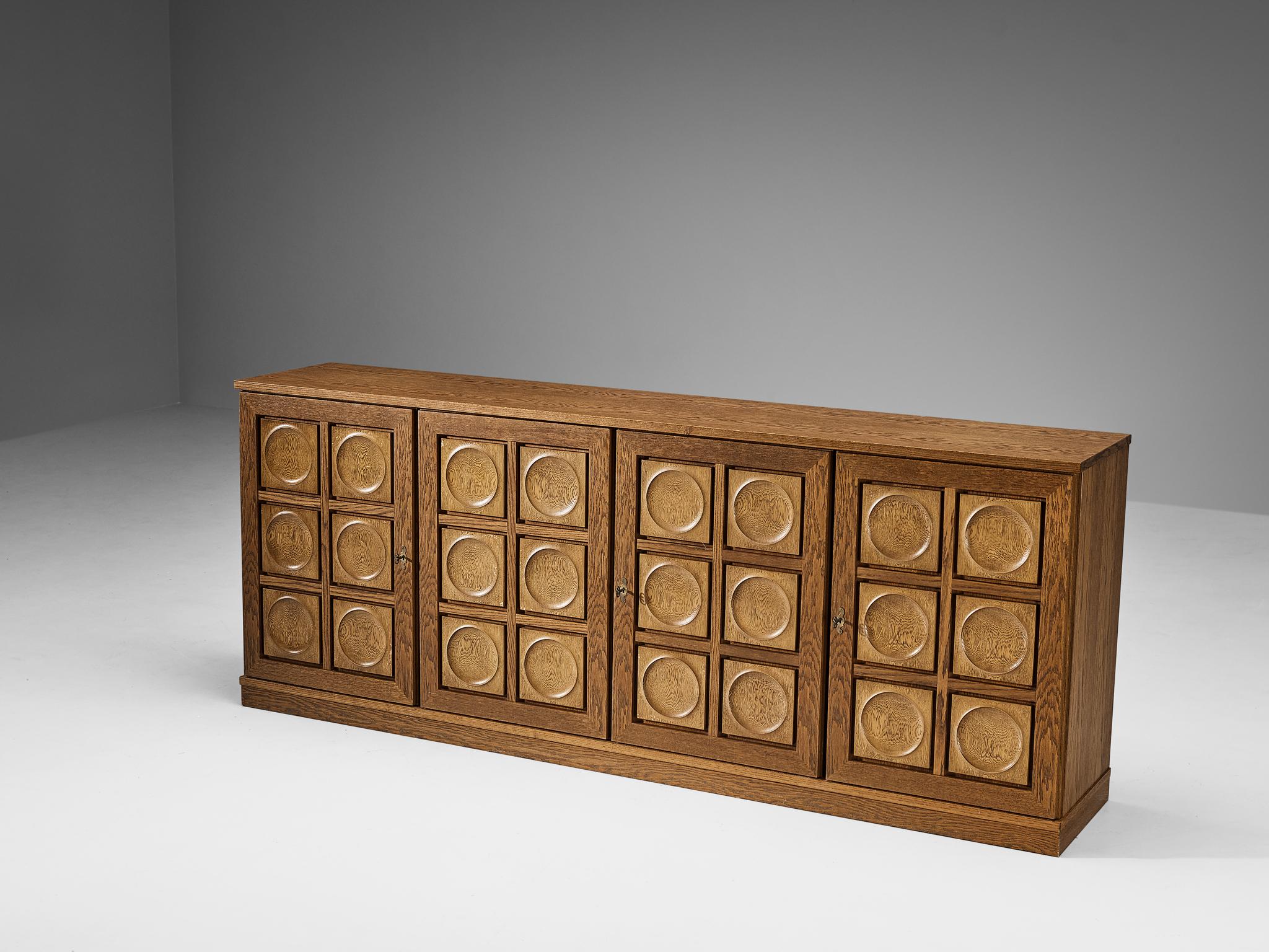 Sideboard or credenza, oak, brass, plastic, felt, Belgium, 1970s.

This cabinet features a clear rhythm and flow established by means of a well-thought-out lay out that is utterly well-balanced. The carved circles immediately catch the eye and are