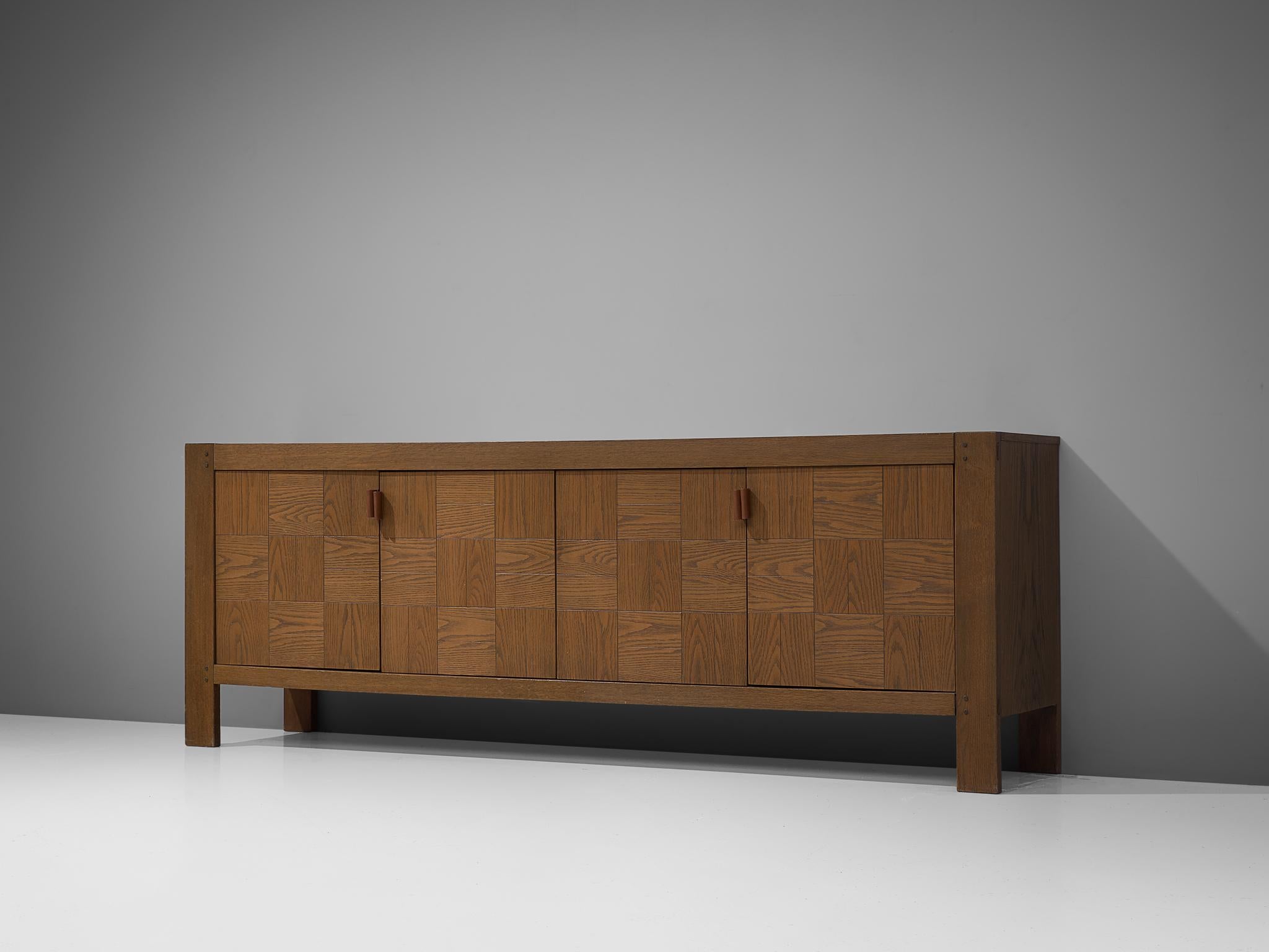 Sideboard, oak, Belgium, 1970s

Brutalist sideboard executed in oak. The decorative doors are finished in way that a patchwork is created with a combination of horizontal and vertical inlayed grained oak tiles. The handles are made of cognac leather
