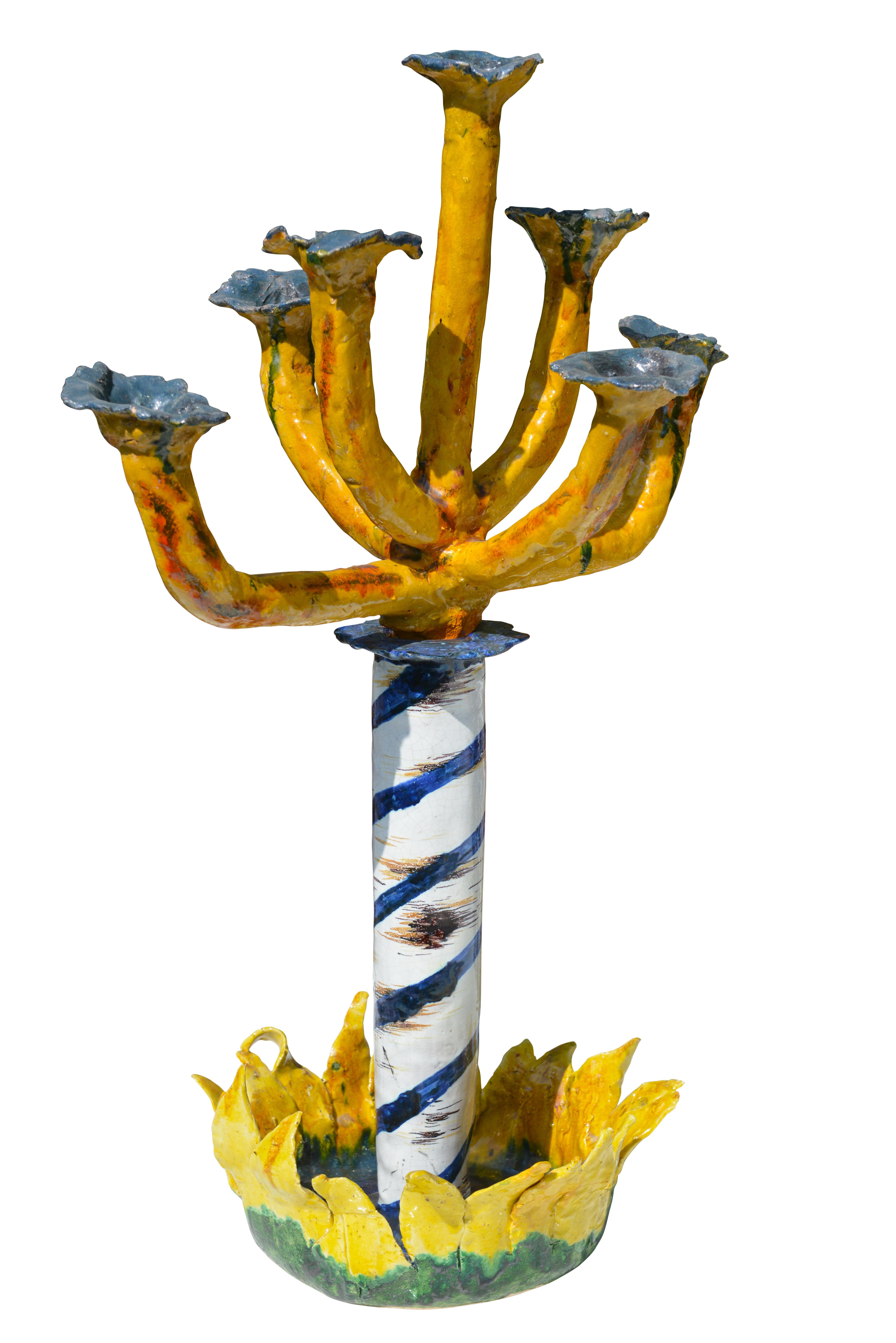 Spectacular and extremely eccentric ceramic candlestick. It is an iconic piece, made by anonymous craftsman. At the base is a stylized sunflower with delicately shaped petals. A central blue and white twisted column supports the seven branched