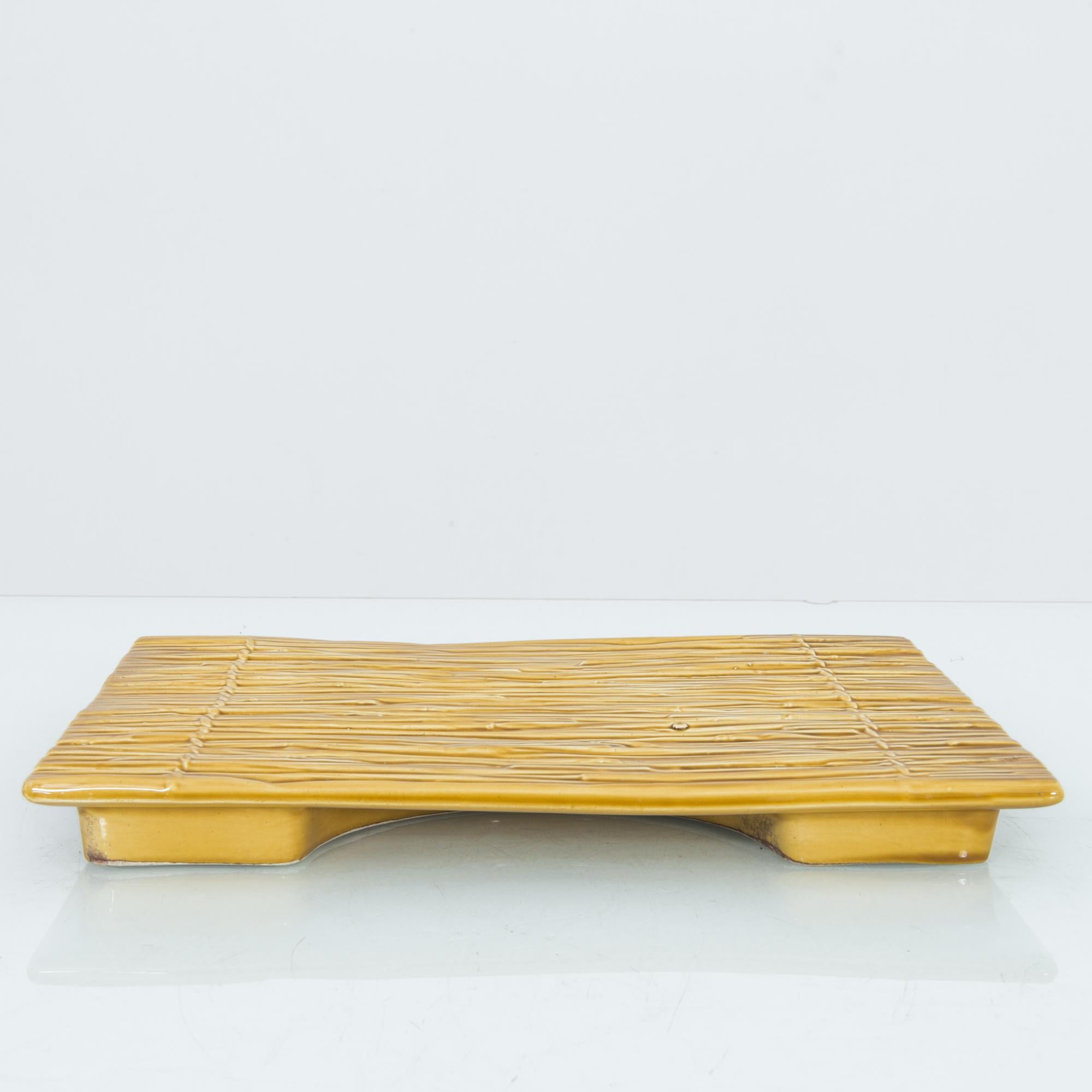 A ceramic tray from Belgium, circa 1950. The tray is glazed yellow in the style of a bamboo mat on a small platform. A glorious bit of kitsch, exuding color and character.