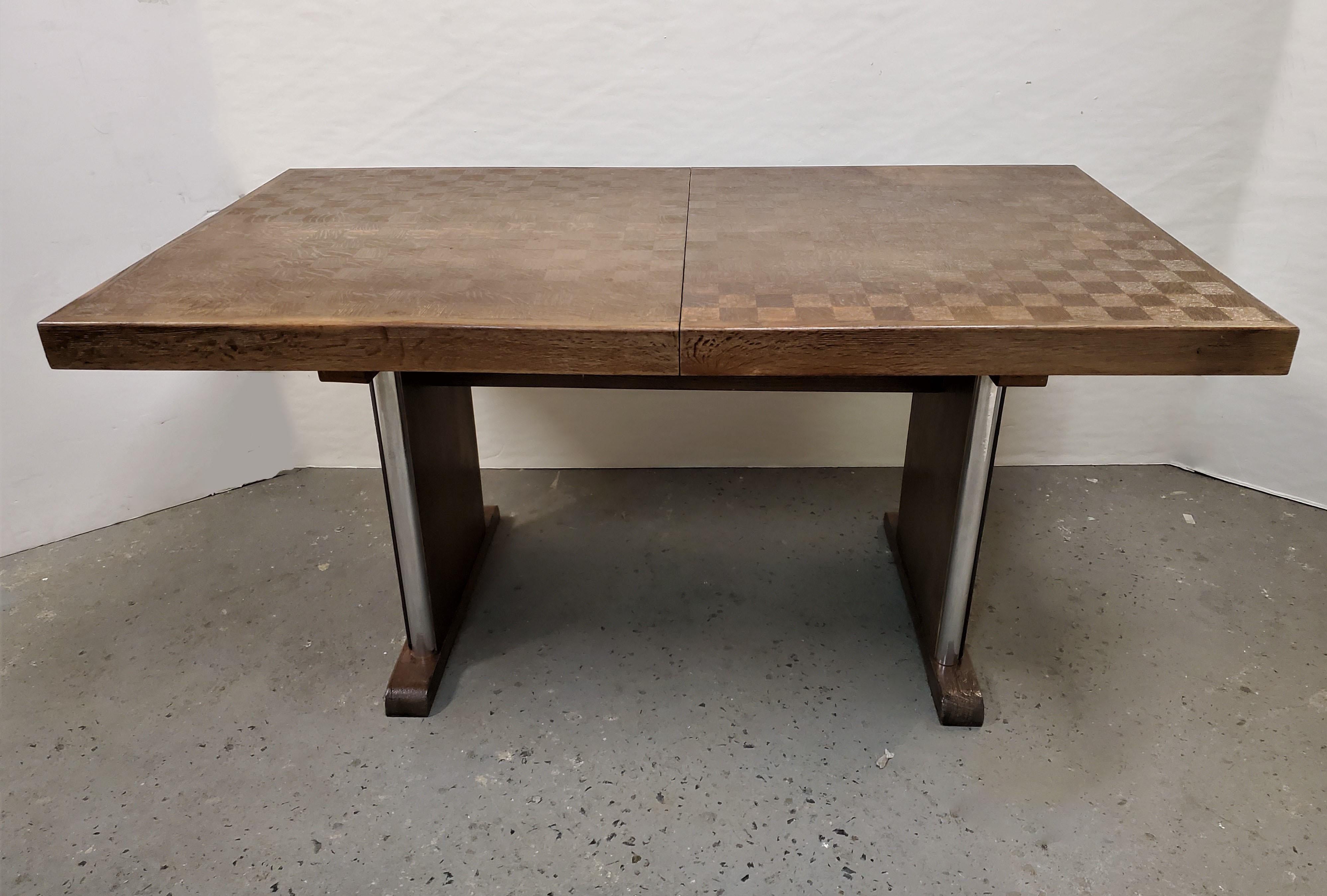 An original Belgian Art Deco dining table featuring a parquetry inlaid table top defined by expert woodworking and a curved double pedestal base with polished aluminum decorative accents. 
Branded 