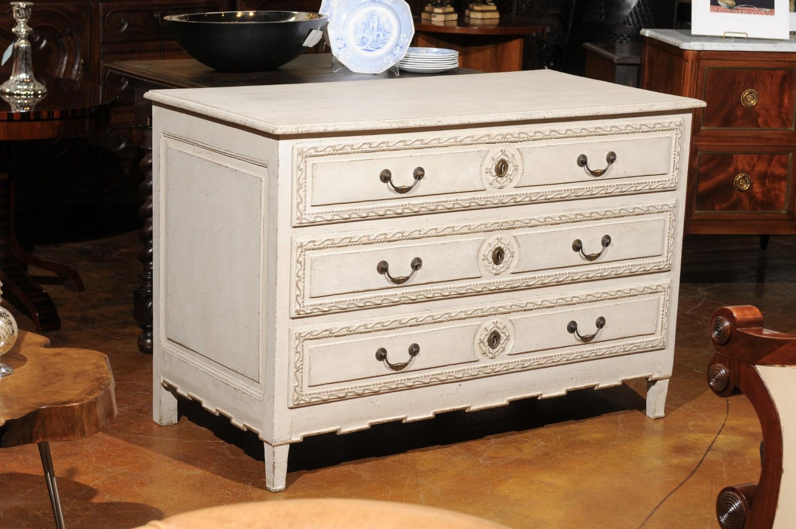 A Belgian Directoire style painted three-drawer commode from the mid-19th century, with carved drawers and elongated dentil molding. Born in Belgium during the 1850s, this painted commode features a rectangular top with beveled edges, sitting above