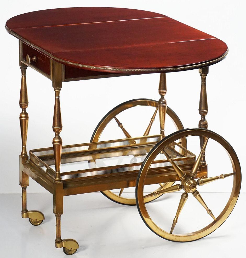 A handsome vintage Belgian rectangular bar cart table or serving trolley from the mid-20th century design era, featuring a table-top frieze of mahogany with two drop leaves and a drawer with decorative bronze accents and hardware, mounted to a frame
