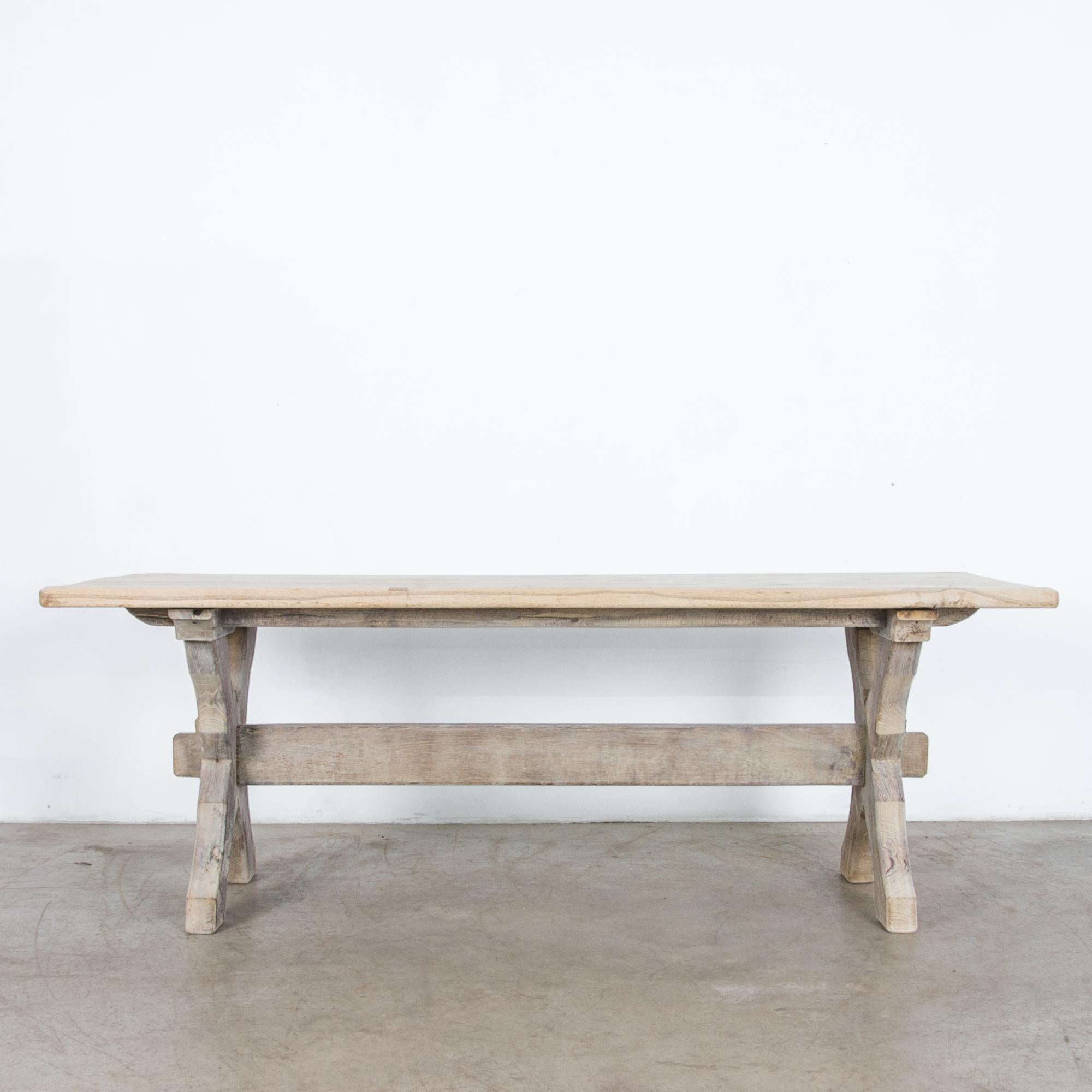 Rustic and simple Belgian style farmhouse table from the 1950s in bleached oak, features distinct crossed legs and trestle brace. Simple wooden forms recall the countryside ideal, following the lineage of European craftsmanship, with modernist