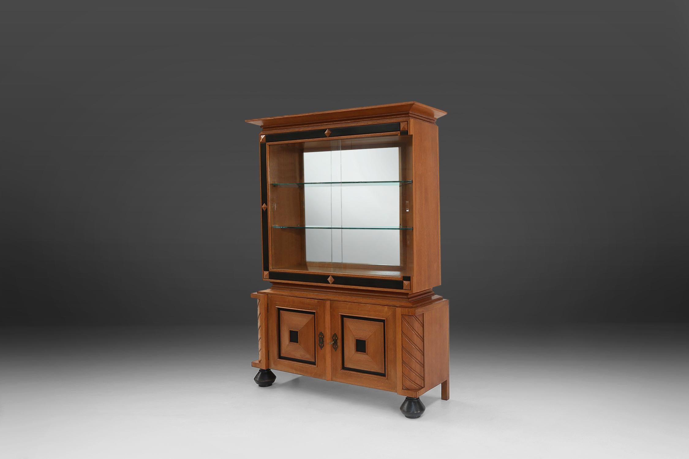 Robust cabinet features two square door panels, above these doors there is a vitrine.

A beautiful detail that makes it such a well-designed piece, are the black round legs. The black details are also reflected in the doors.