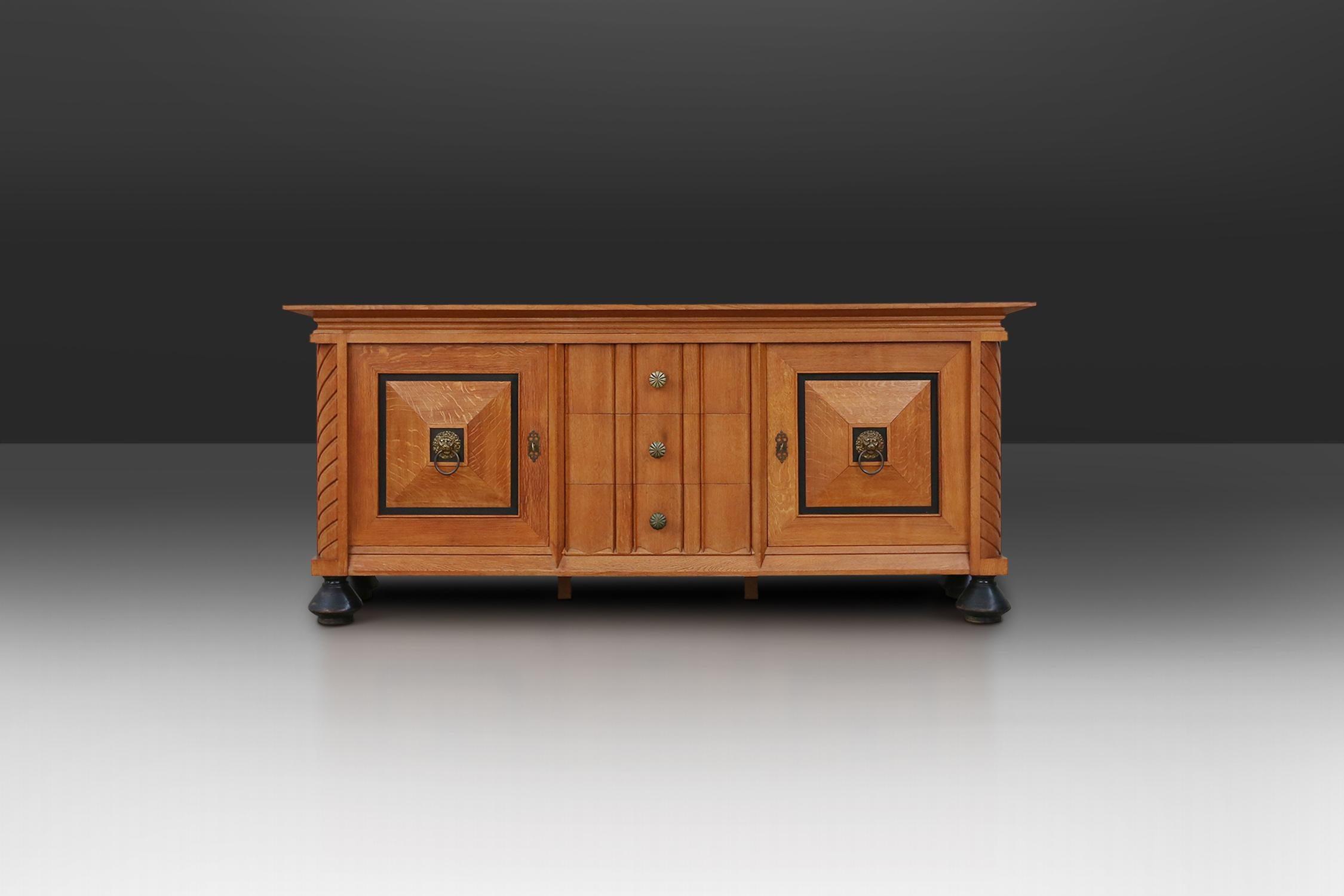 Robust sideboard features two square door panels with a brass lion head. in the middle three large drawers with brass handles.

A beautiful detail that makes it such a well-designed piece, are the black round legs. The black details are also