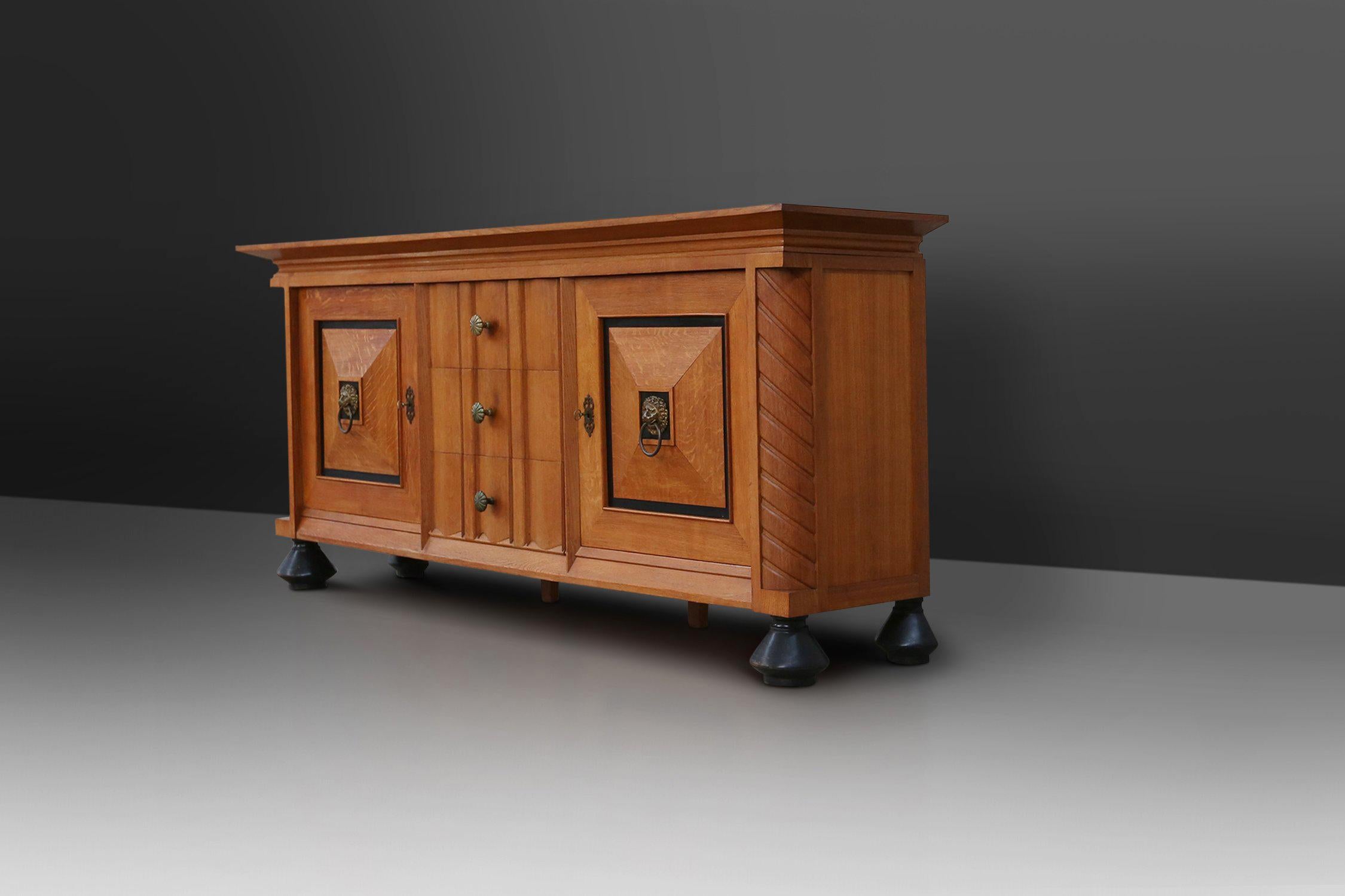 Belgien / 1940 / Anrichte / Eiche, Messing / Art Deco

Robustes und dekoratives Sideboard aus Eiche mit schwarz lackierten Details und Messinggriffen. Dieser Schrank hat zwei quadratische Türen mit Paneelen und jeweils einem Löwenkopfgriff aus