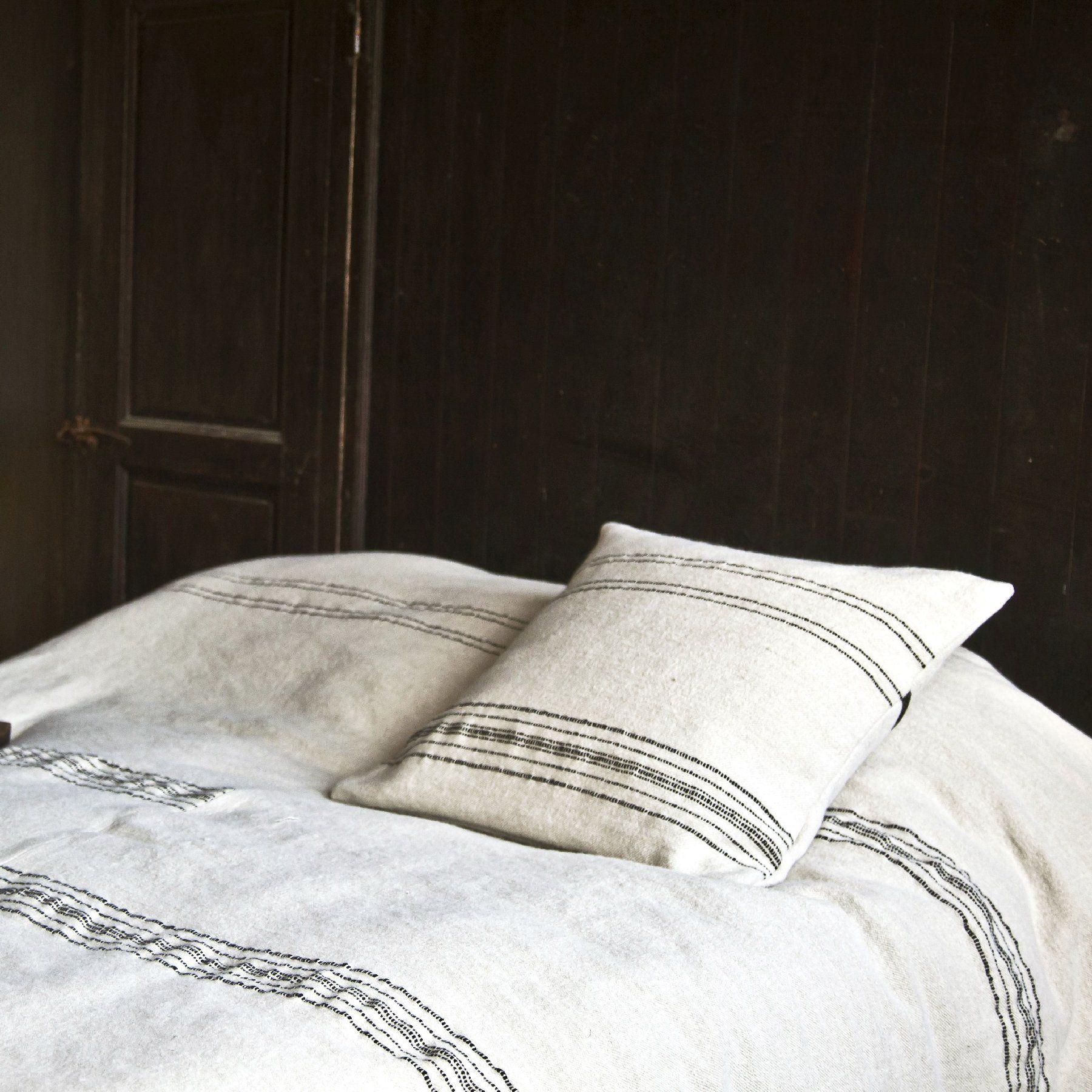 Inspirés des couvertures marocaines trouvées sur les marchés, ces couvre-lits sont constitués de deux pièces cousues ensemble au centre, créant des rayures noires asymétriques sur un fond d'os solide. Les mêmes rayures se retrouvent sur le devant