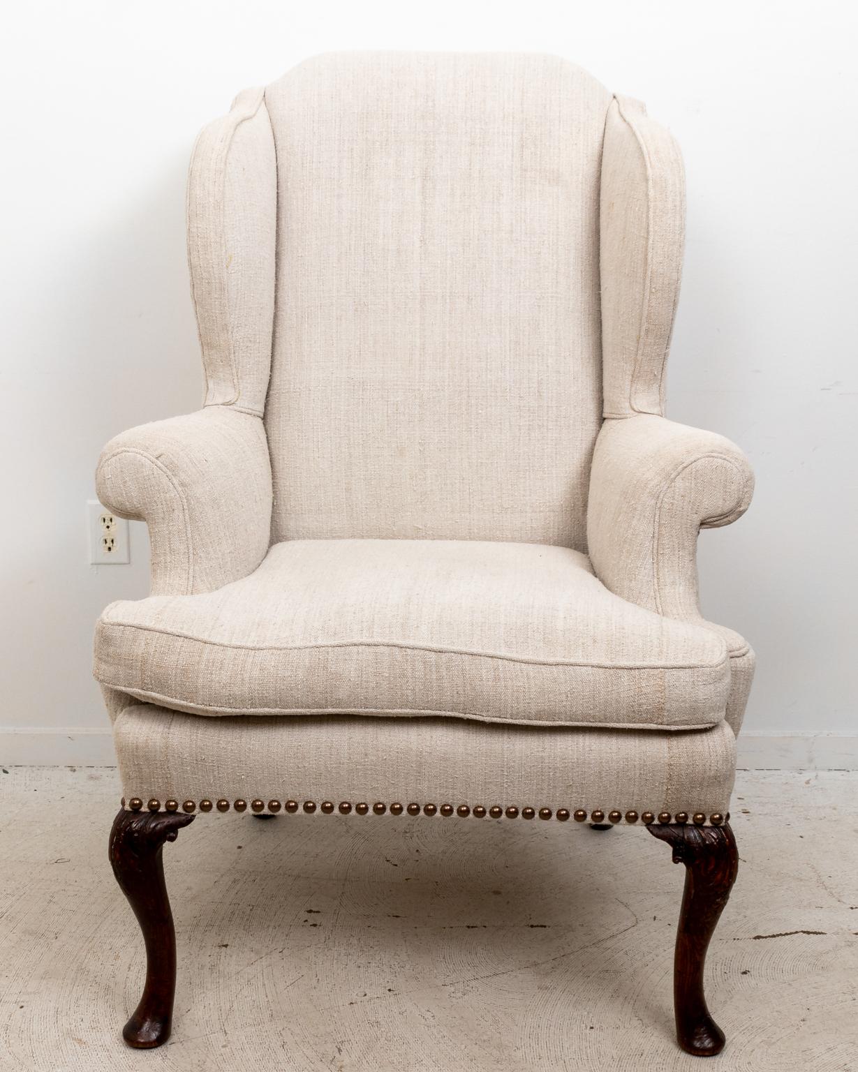 English style wing back armchair upholstered in a Belgian linen with cabriole legs, pad feet, and metal nail head trim. Please note of wear consistent with age.