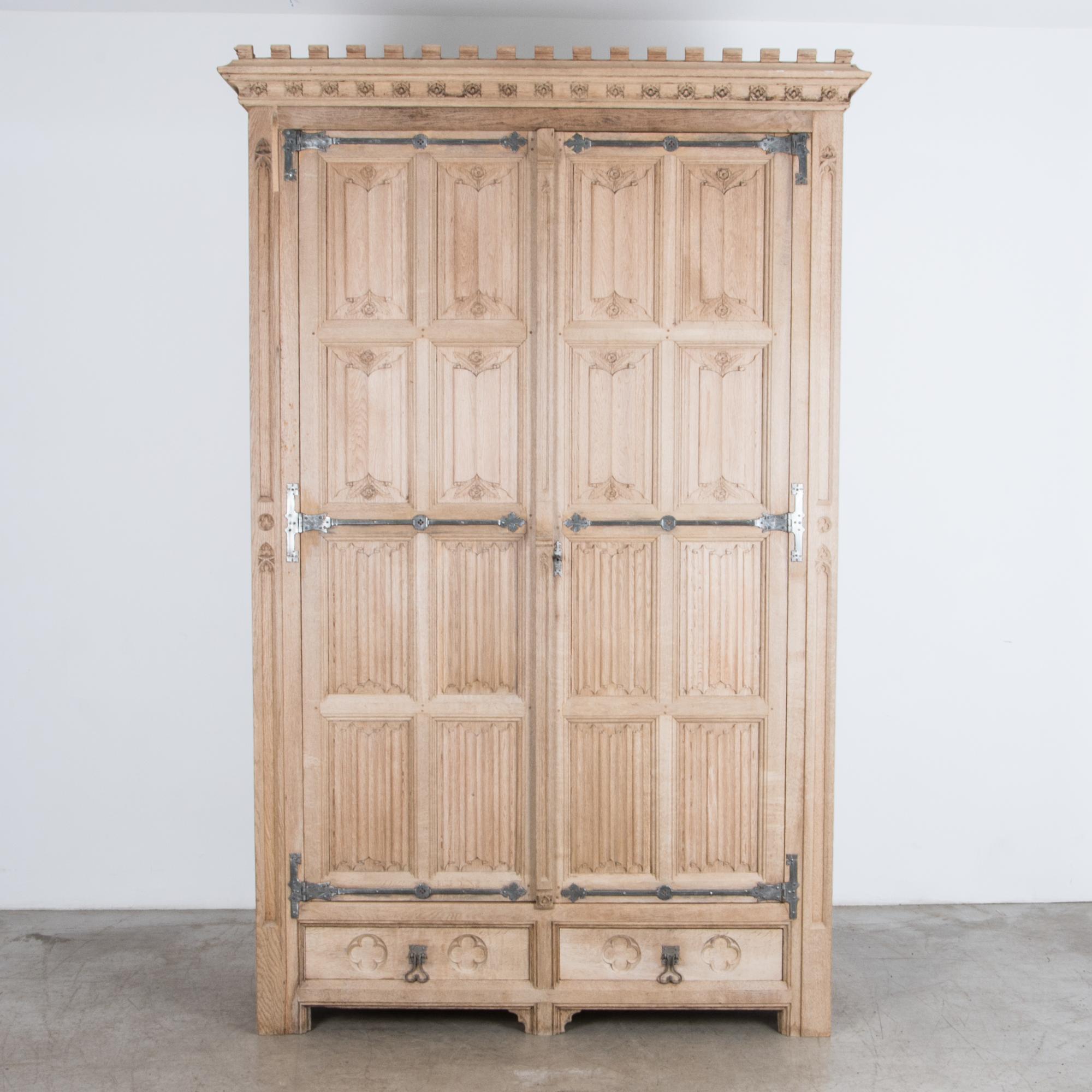 A French influenced wardrobe from Belgium, circa 1900. With an eclectic mix of styles this sturdy oak cabinet features a carved fabric motif, mixed with gothic elements and rustic iron hardware. Rustic proportions give plenty of storage space, with