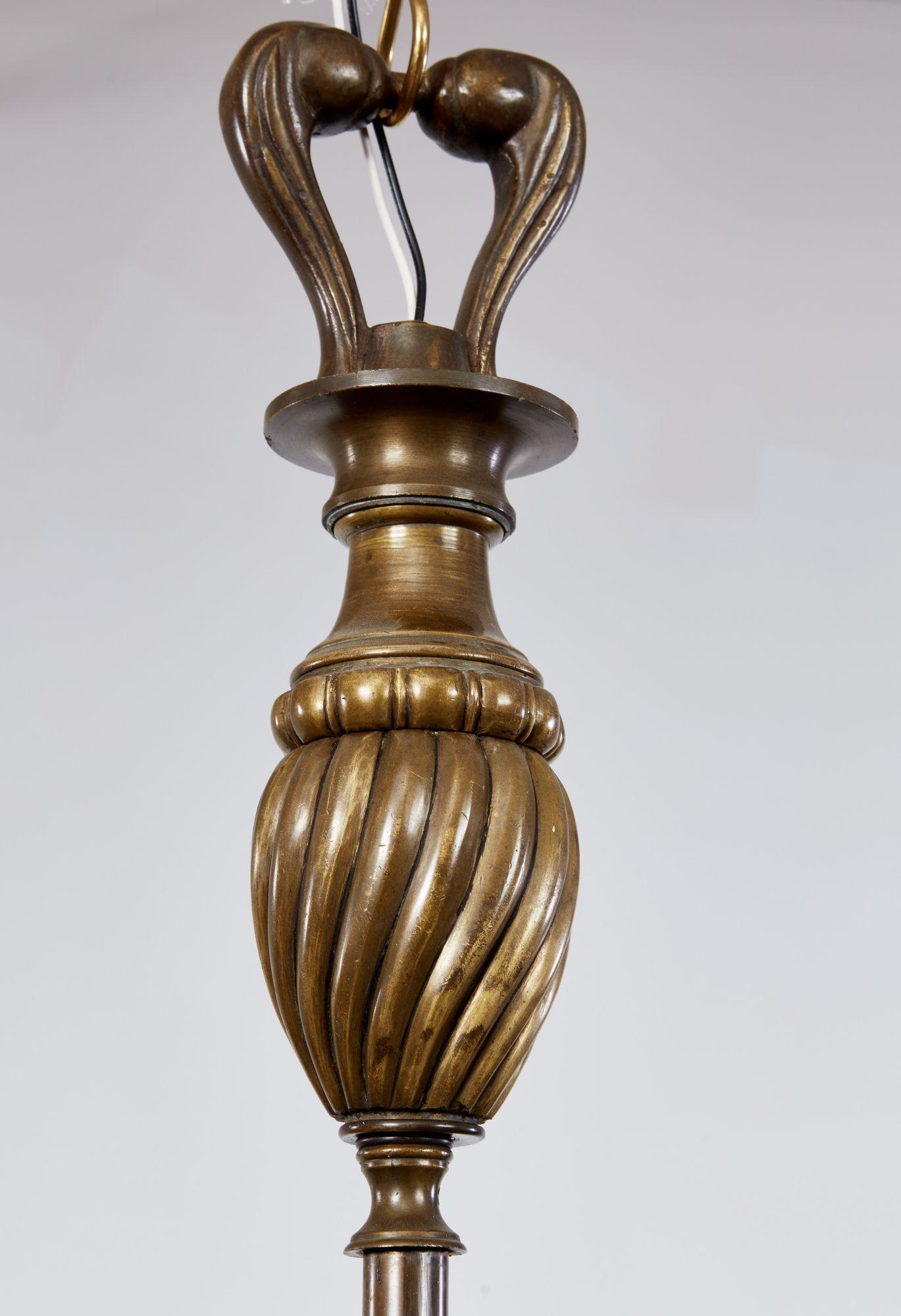 Insolito lampadario belga a otto luci, 1930 circa, con albero centrale con vaso scanalato a spirale e otto bracci con fiori di loto stilizzati che spuntano da un unico cesto con canne e lobi, il tutto con una ricca patinatura e una forma aggraziata.