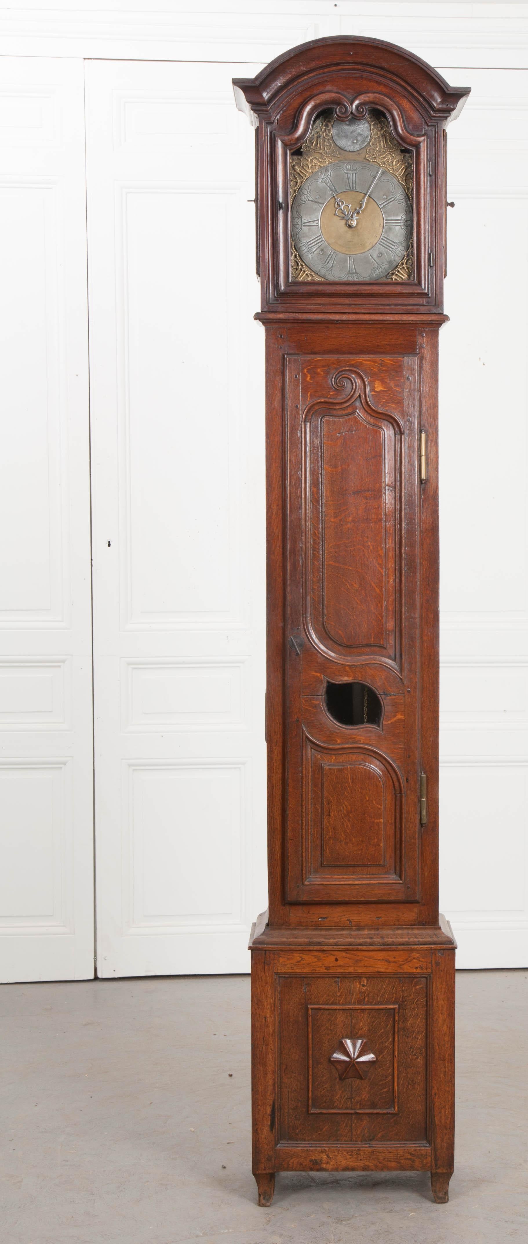 This lovely antique oak tall case clock was created in Belgium, circa 1800s or earlier, and retains all of its original hardware. The arched and carved bonnet, having a conforming central glazed door and two oak side doors, houses the mechanism with