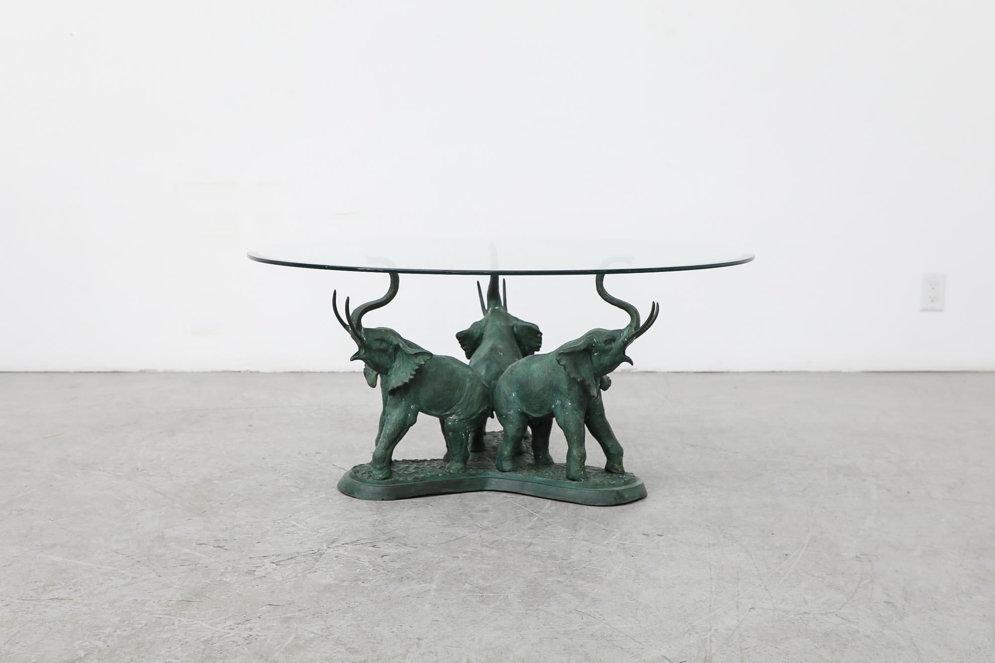 Heavy, 1970s glass coffee table with decorative elephant sculpture base. In original condition with beautiful, heavy patina on the elephants, consistent with their age and use. Another sculptural coffee table is available and listed separately