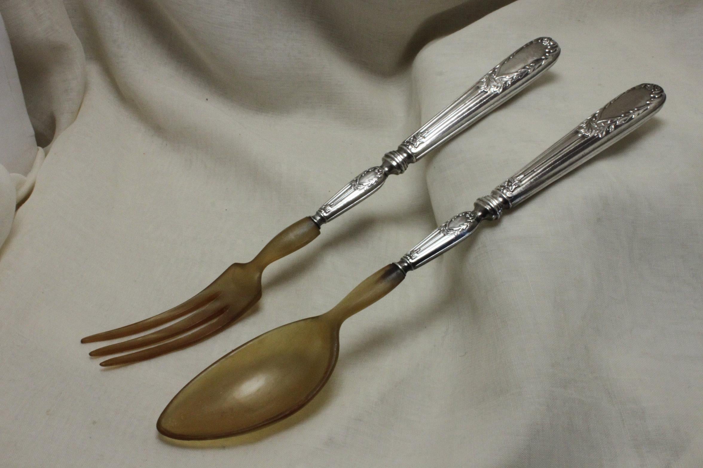 The handles of this pair of very attractive silver and horn salad servers are decorated with neo-classical laurel wreaths atop fluted, tapering columns, which contrast nicely to the plainness of the spoon and fork. The handles carry the mark 950M