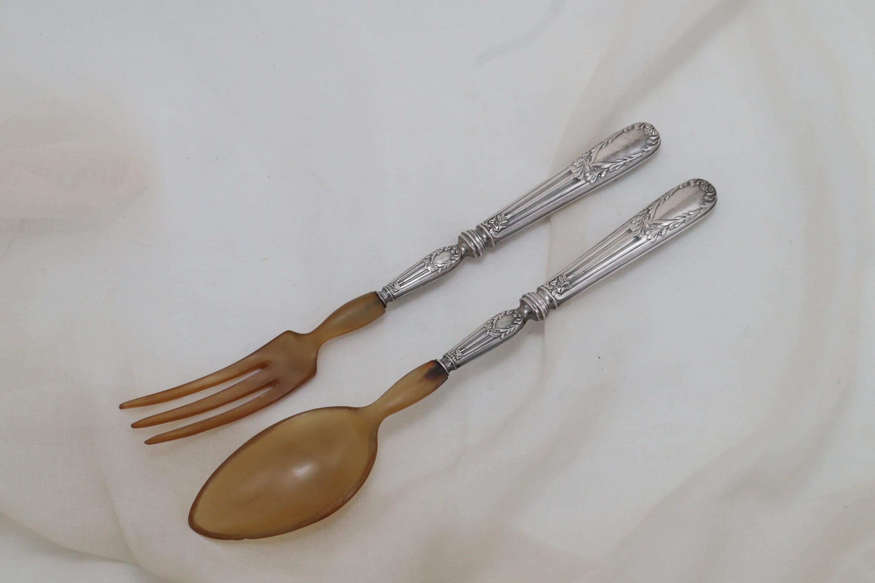 The handles of this pair of very attractive silver and horn salad servers are decorated with neo-classical laurel wreaths atop fluted, tapering columns, which contrast nicely to the plainness of the spoon and fork. The handles carry the mark 950M