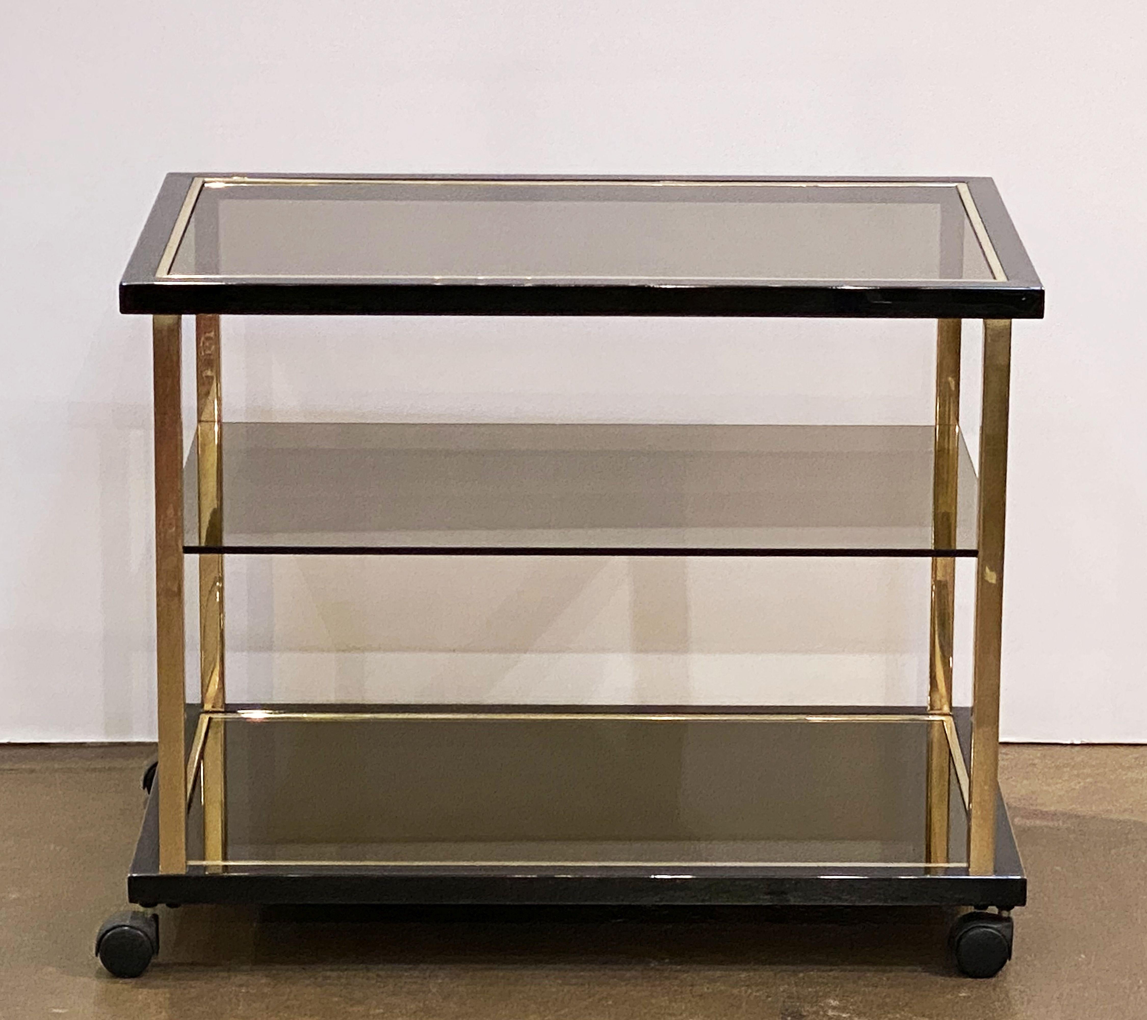 A fine Belgian rectangular three-tier drinks cart (bar cart) or trolley server by Belgochrom, featuring a stylish brass and steel frame with inset smoked glass panels on rolling casters.

Makes a great side or occasional table.

Dimensions: H 26