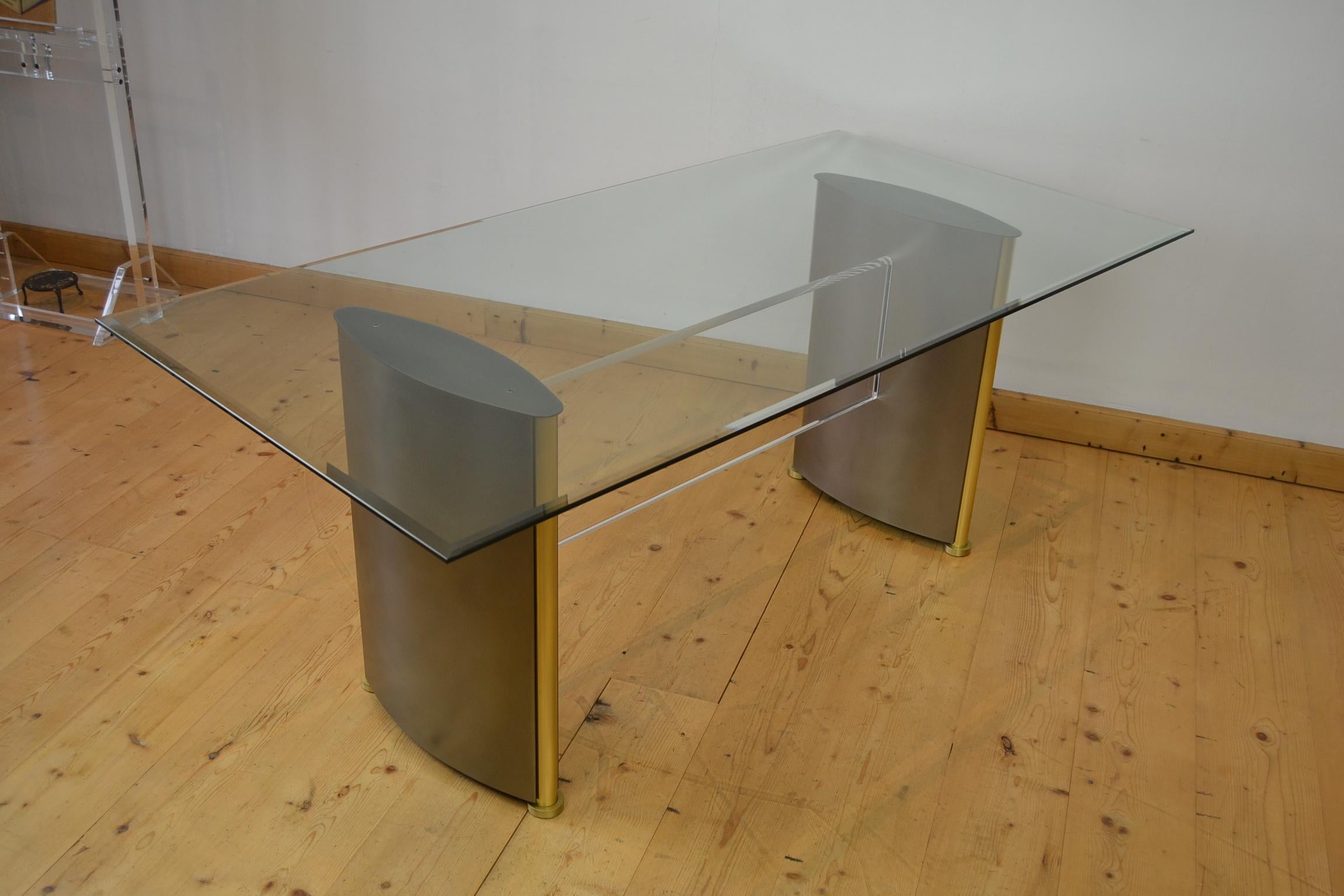 Belgo Chrome dining table. 
This stylish Hollywood Regency Belgochrom table has 2 bronzed patinated metal legs with gold-plated brass details which are connected by a lucite connecting piece. On top you find a thick beveled glass top.
The size of