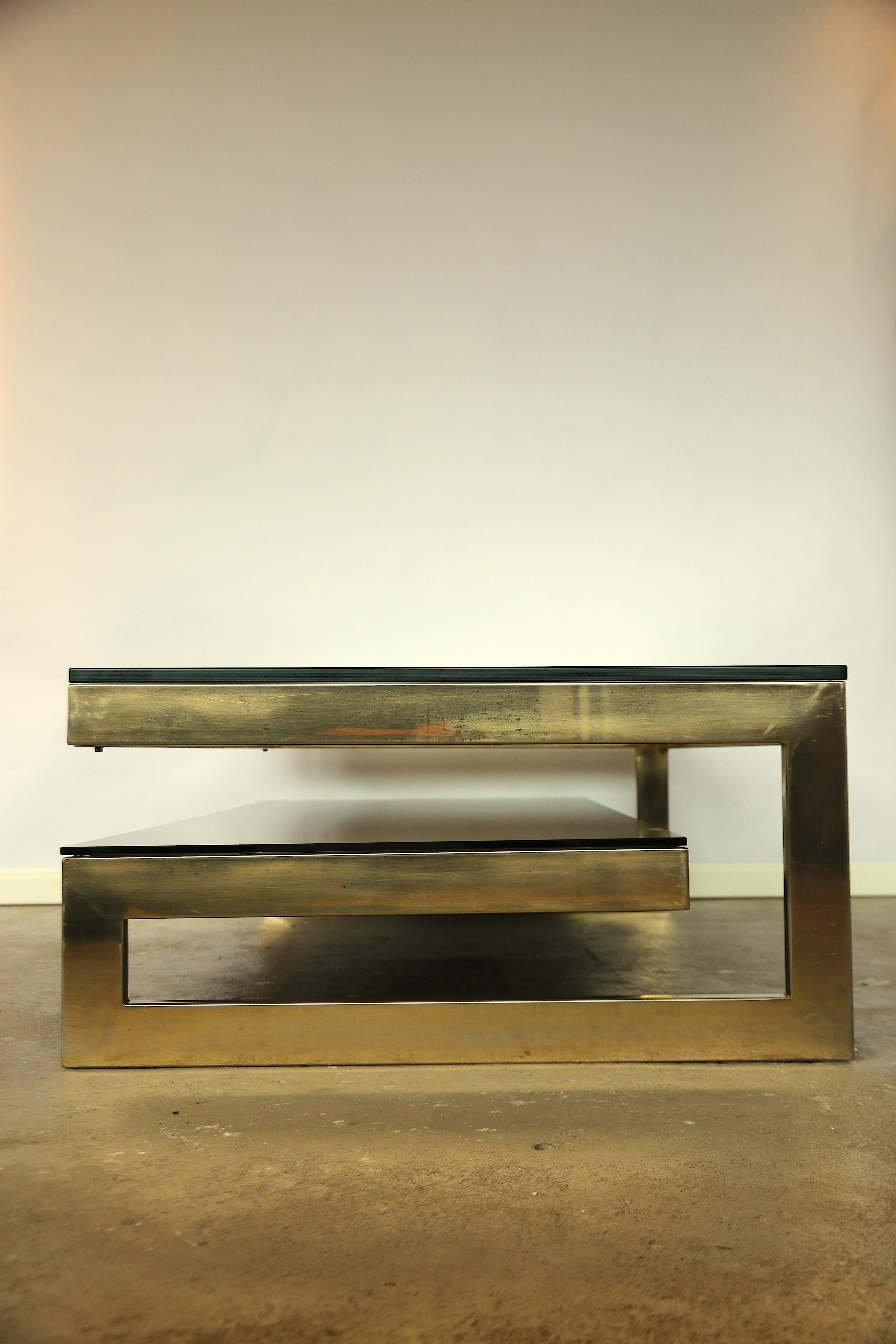 Stunning Hollywood Regency style very chic G shaped 2-tier coffee table. There are in total 3 identical available, of which all have their layer of (real) 23-carat gold still very thick and shiny on them. The bronze glass mirror and glass top are