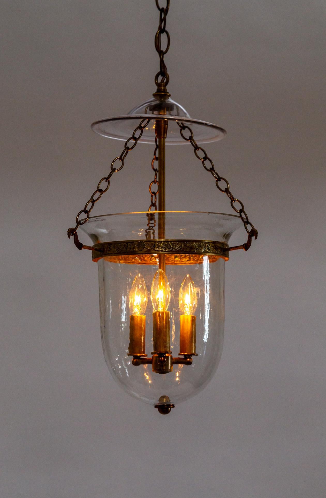 A lovely lantern made with an antique blown glass bell jar and smoke bell. The brass details- decorative etched rim, chain, stem, finial, and candle covers make a refined and cohesive look. 3 candelabra lights. It is newly made with antique glass.