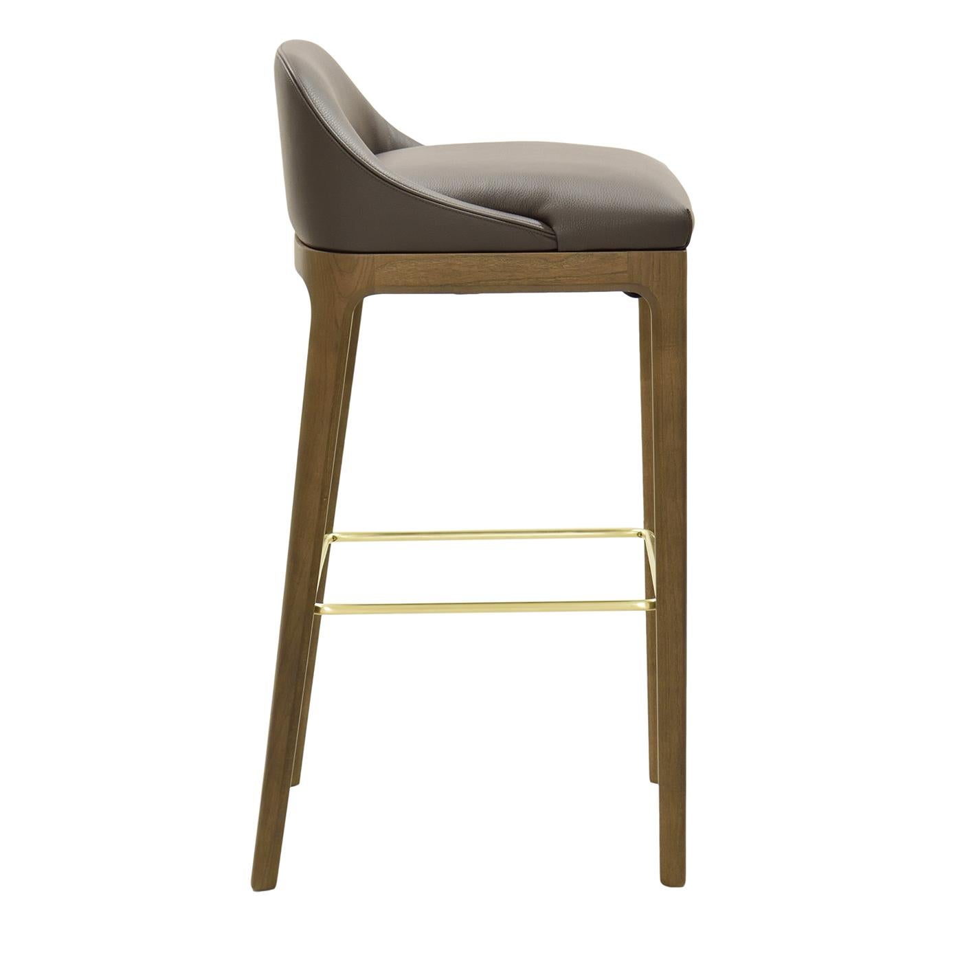 This polished bar stool in ash combines a modern aesthetic with high comfort, provided by its plush padded seat. Showcasing a harmonious silhouette, this exclusive stool stands on four straight legs connected by a metal footrest with a gold glossy