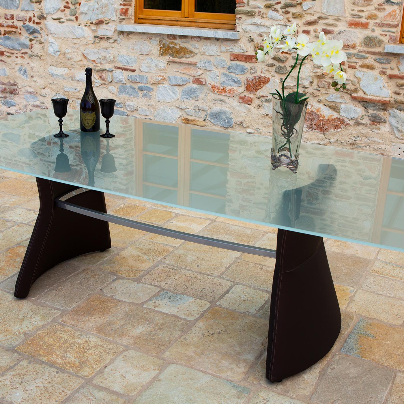 A dynamic interplay between lightness and strength, fragility and robustness, this modern dining table boasts a rectangular top with beveled edges. Made of glass, the top is sustained by a steel structure and two slanted, thick legs. This exquisite