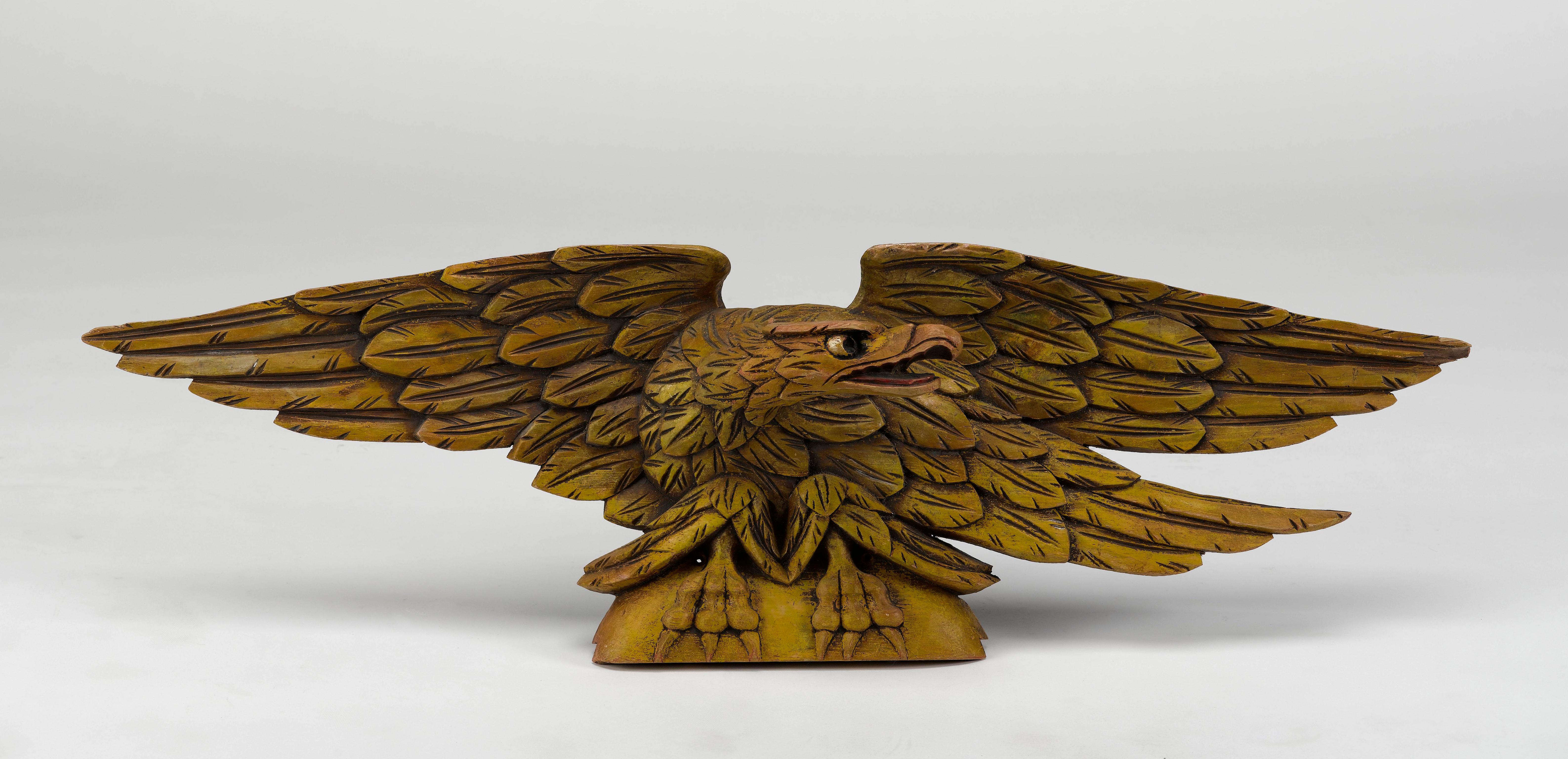 This is an original American eagle, hand-carved from pine during the early to mid 20th century. The eagle features a touch of original gilt over yellow sizing with hand-painted highlights, emphasizing the eyes and beak.

The eagle is displayed with
