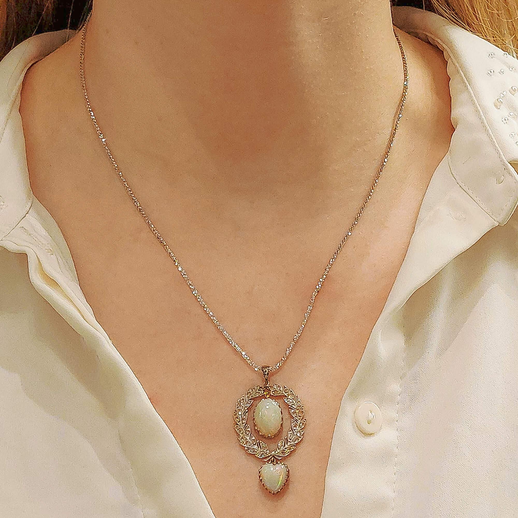 A Belle Epoque opal and diamond pendant in platinum and gold, featuring an oval cabochon white opal claw-set on a platinum open-back scalloped collet, suspended from a rose-cut diamond-set platinum wreath that surrounds it, atop a similarly-set