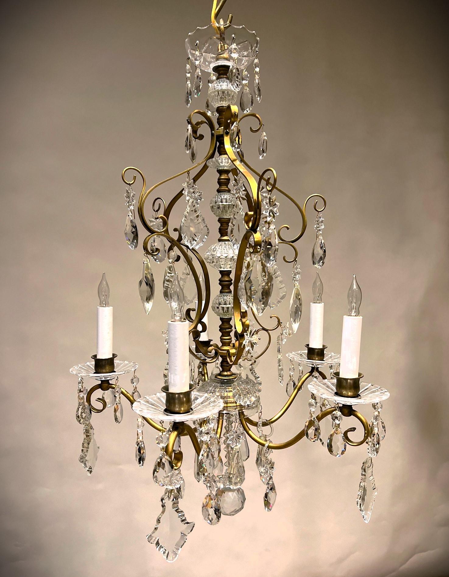 This charming early 20th Century Rococo style chandelier is the perfect size for a foyer or small living or dining room. The frame is hand-cast and -shaped brass with hand-cut crystal components. The fixture has a lovely patina and its crystal has