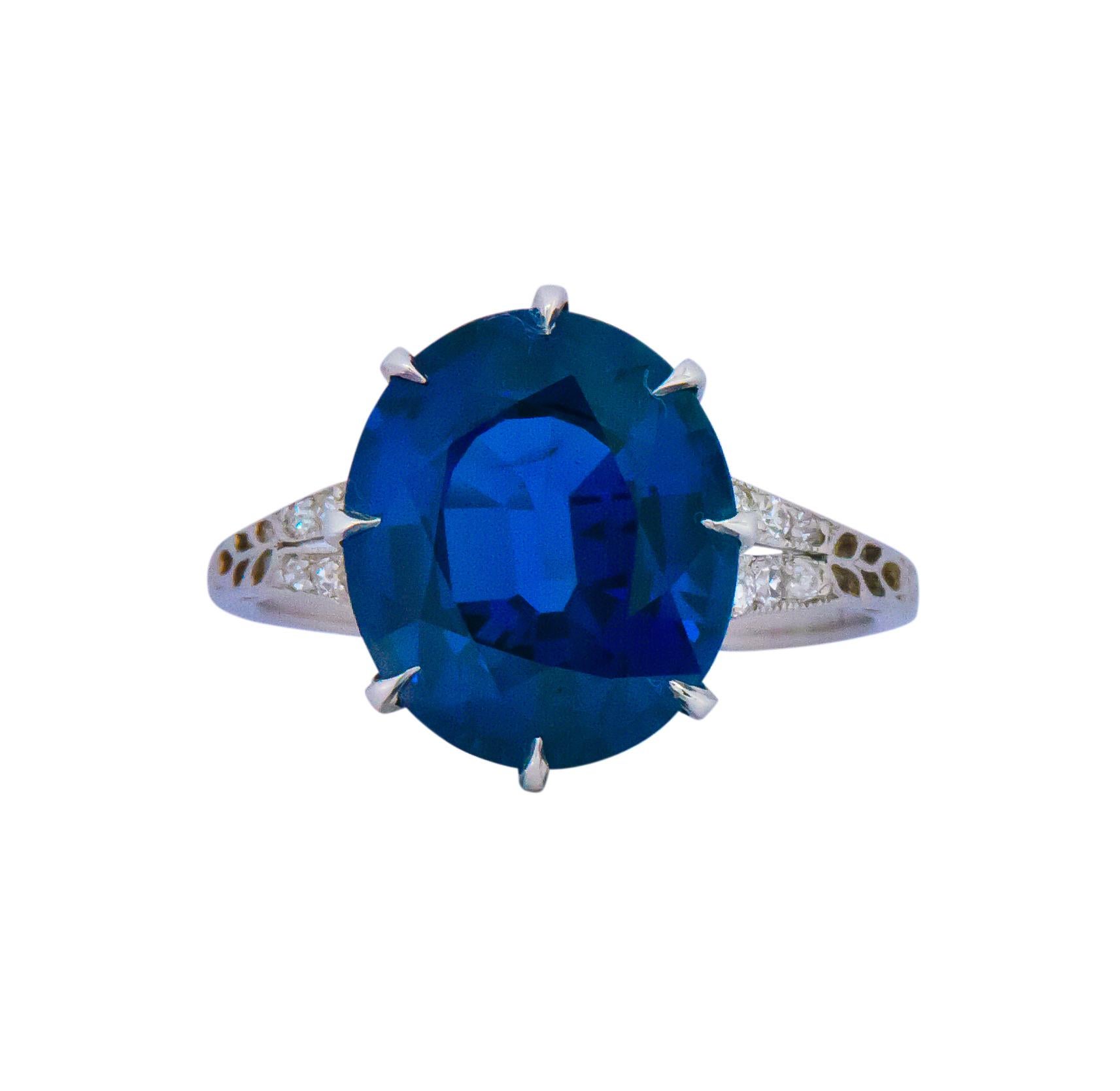 Centering an oval natural royal blue sapphire of intense color weighing 6.51 carats and securely set with 8 claw prongs

Numerous round diamond accents encircle the lower edge of the gallery which also features scrolled platinum designs hugging the