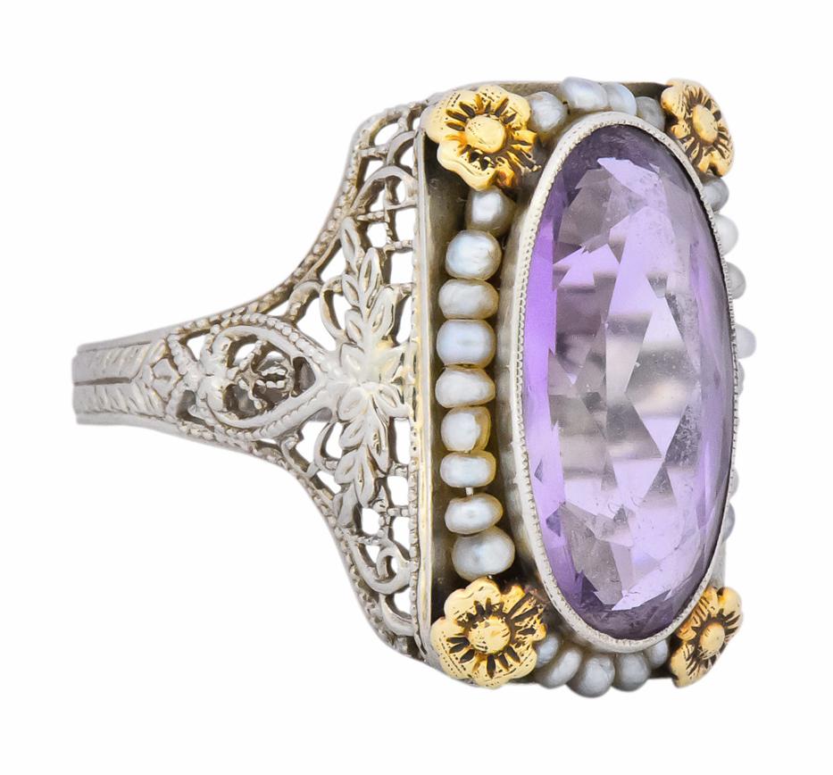 Centering a bezel set oval cut amethyst measuring approximately 15.1 x 7.4 mm, medium-light purple in color

Surrounded by seed pearls with four yellow gold flowers at each corner of rectangular mount

With a pierced floral and foliate lattice