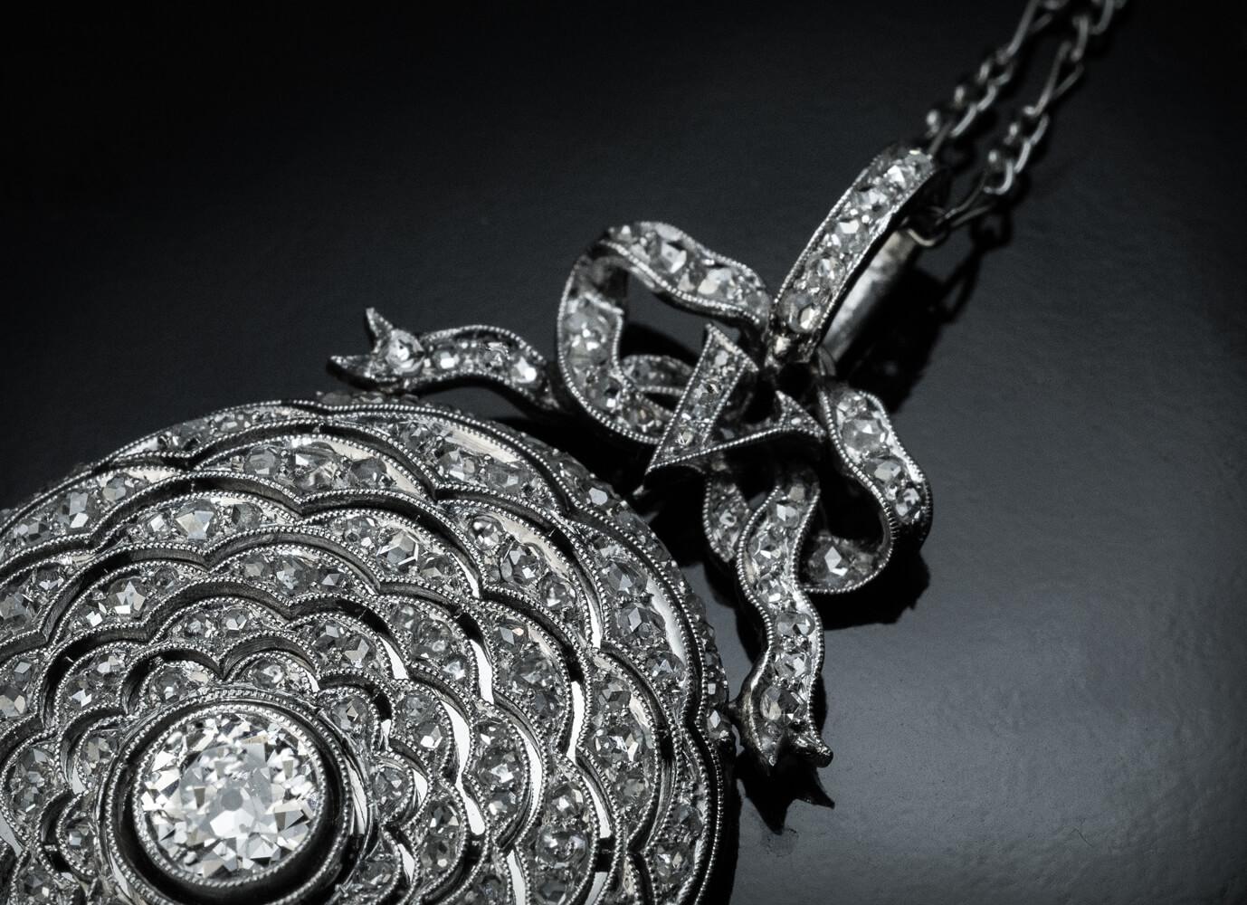 Circa 1910
This superbly crafted fifth anniversary necklace is made entirely in platinum. The front of the pendant is designed as stylized floral petals arranged in concentric circles. The “petals” are set with old rose cut diamonds and applied over