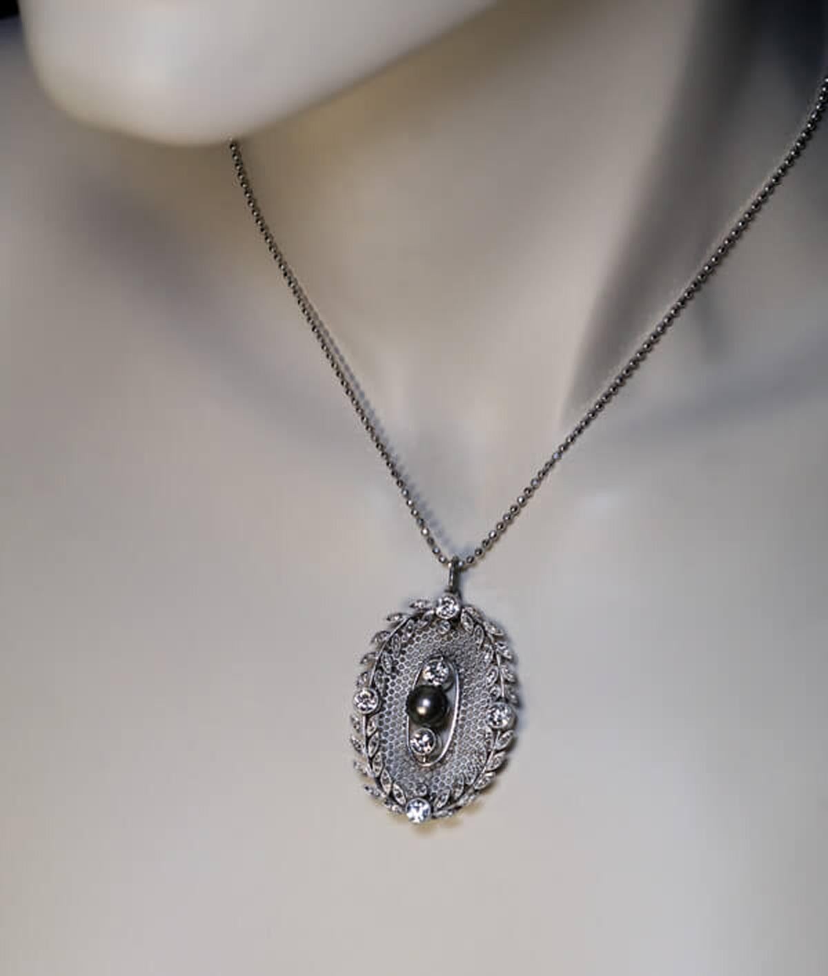 Circa 1910

This antique handcrafted platinum pendant is centered with a 7 mm natural greenish gray pearl vertically flanked by two old European cut diamonds, all of which are inserted into an openwork honeycomb oval panel surrounded by a garland